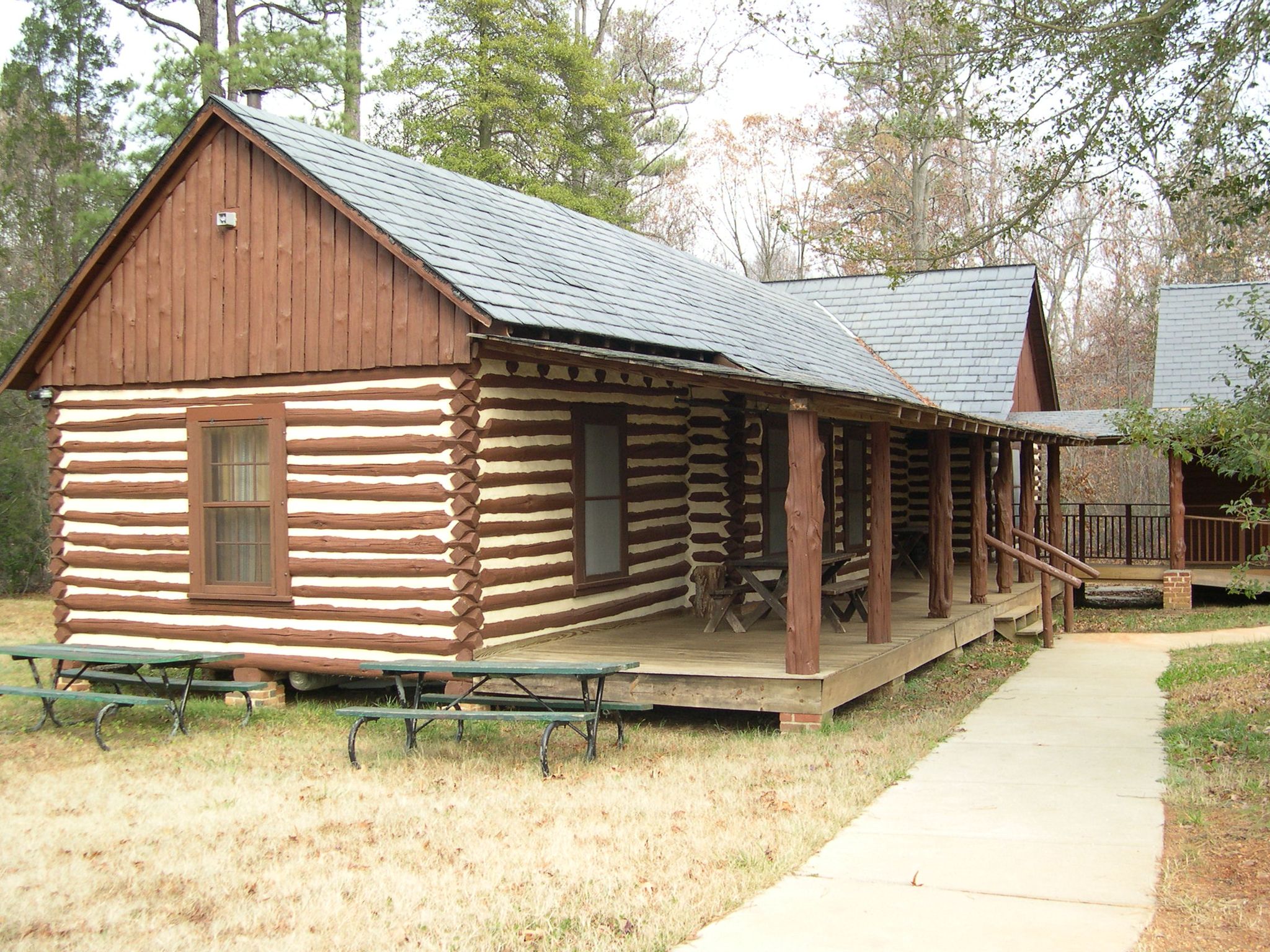 A rustic log cabin with a long porch and picnic tables under diffused light. - Virginia Capital Trail: Osborne Boat Landing Loop