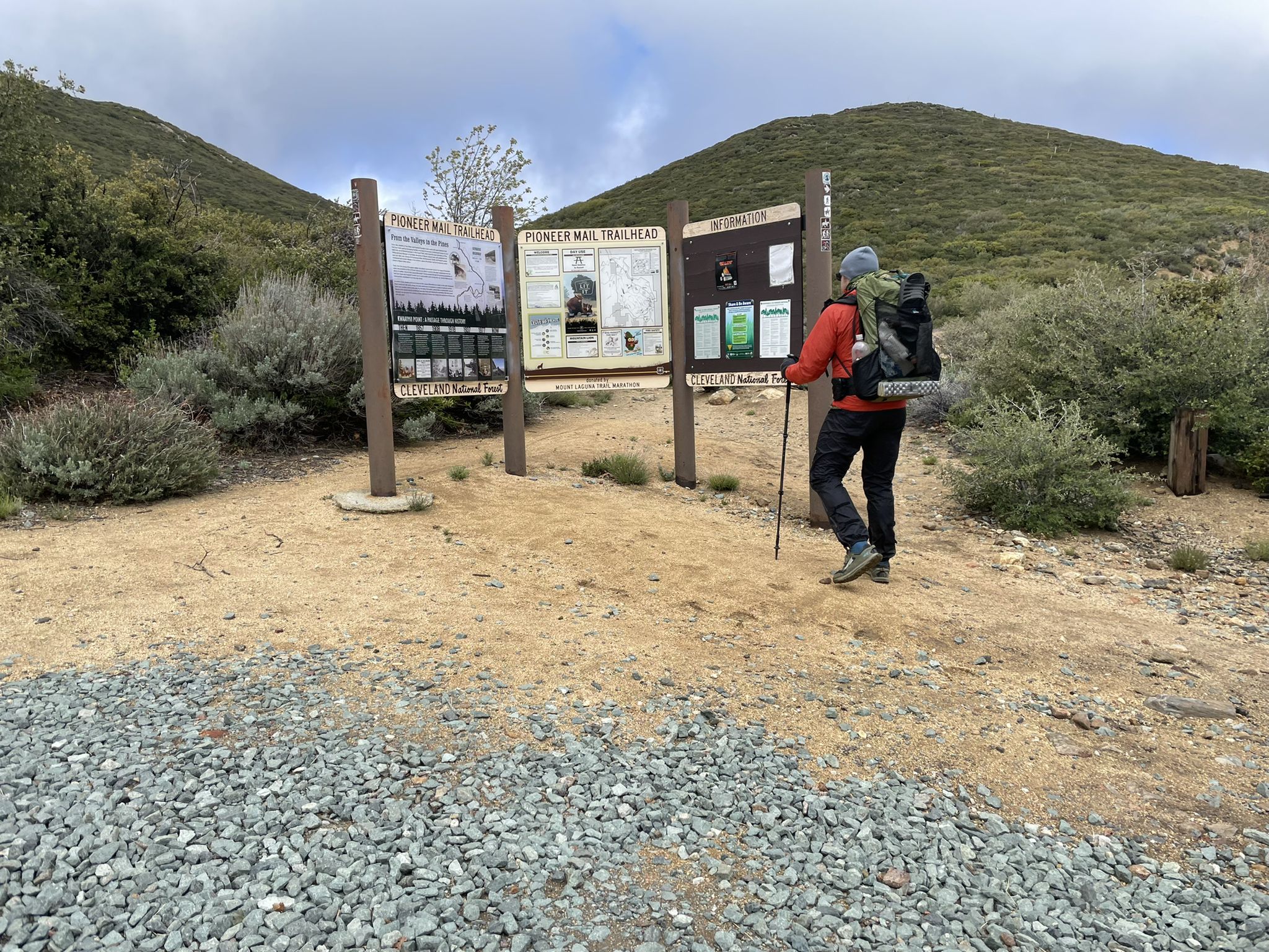 A hiker with a backpack reads trail signs on an overcast day. - Garnet Peak Trail