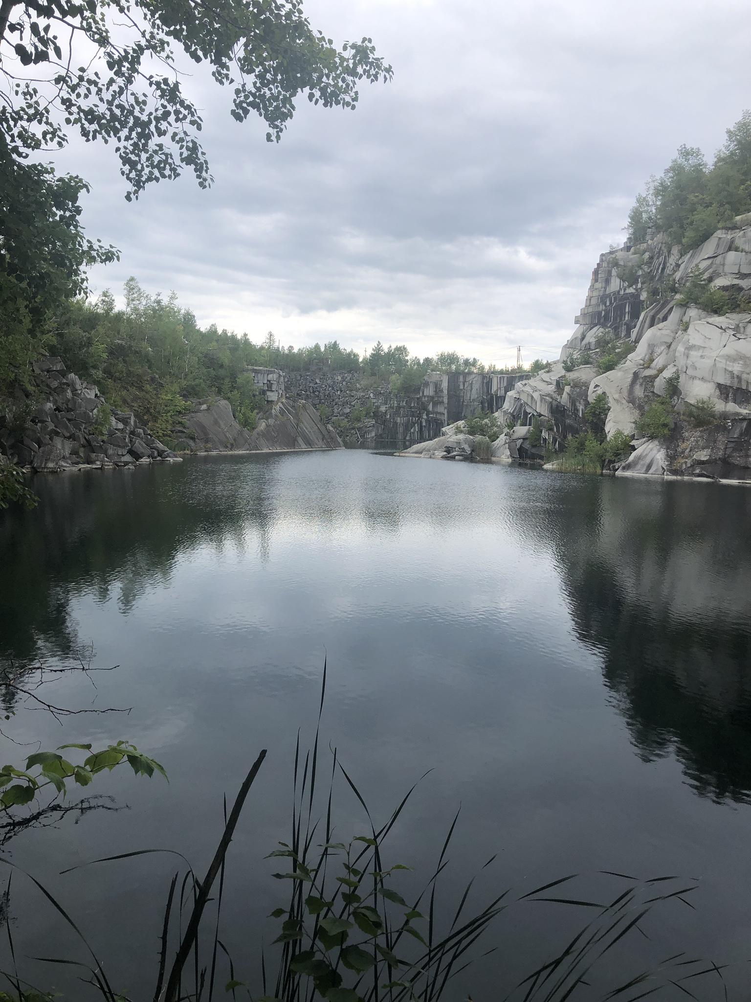 Dark lake surrounded by rocky cliffs and green trees under an overcast sky.