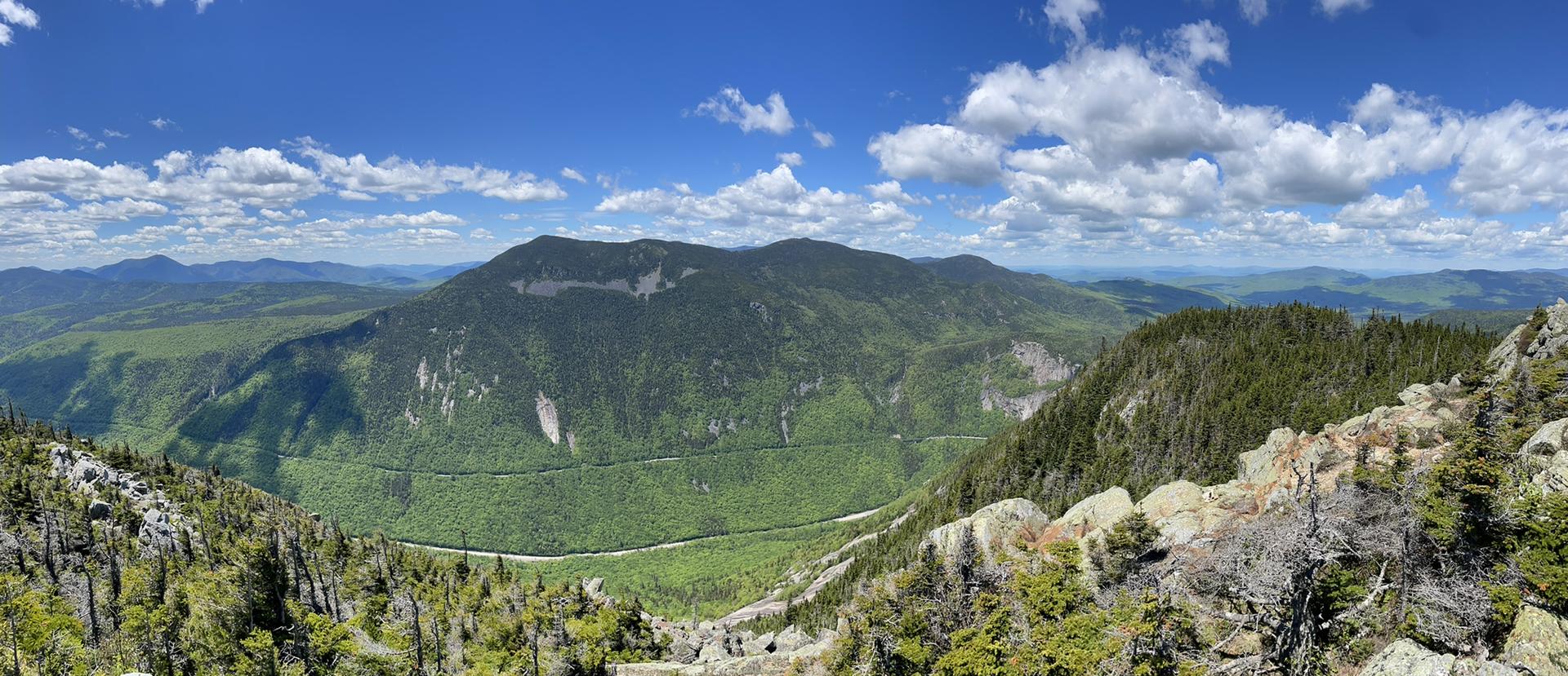 Panoramic view of vast green mountains and valleys under a bright blue sky.