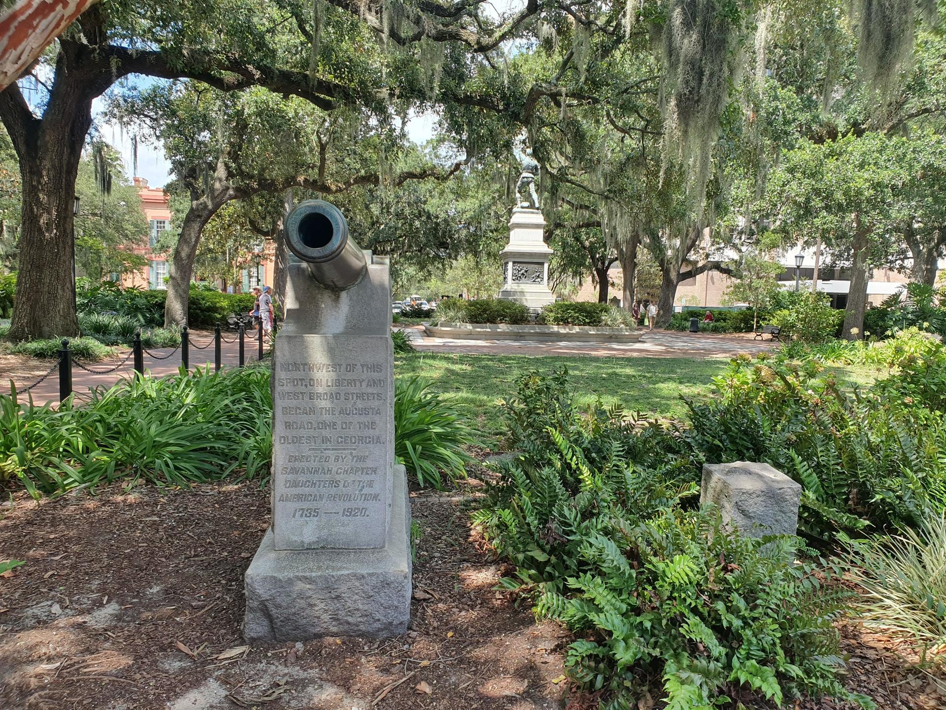 A stone cannon monument sits in a sunny park with lush greenery.