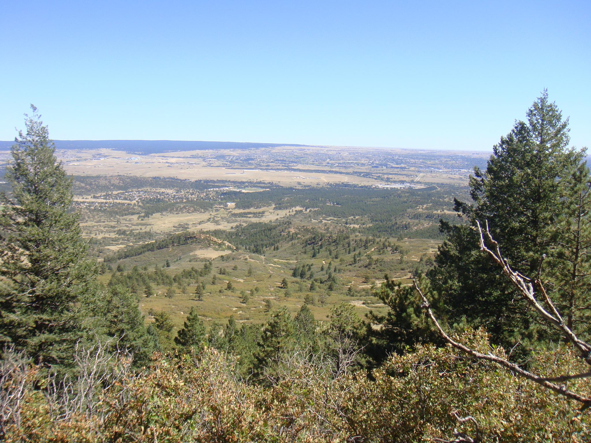 An expansive view of a green, forested valley under a clear blue sky.