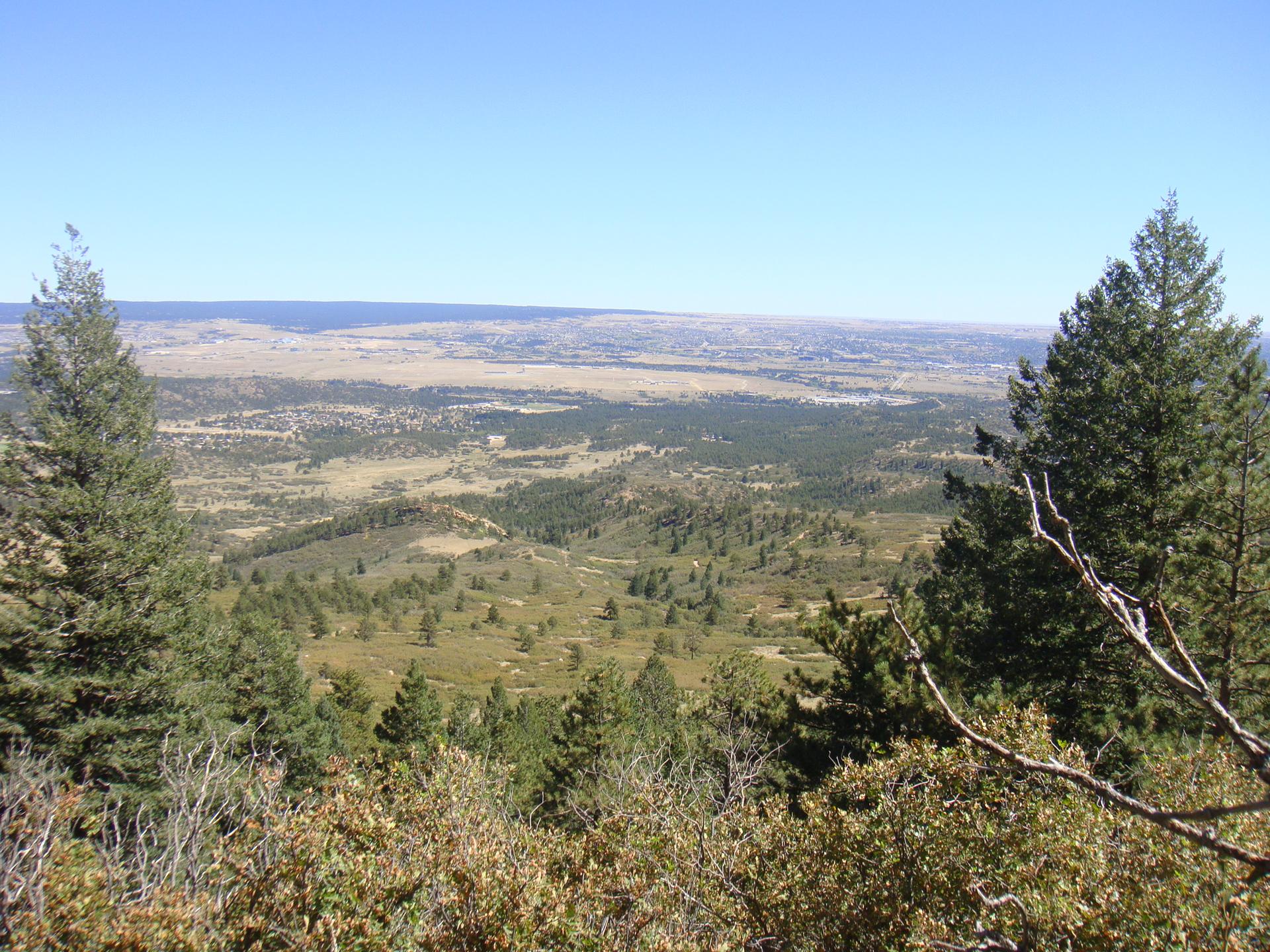 An expansive view of a green, forested valley under a clear blue sky.