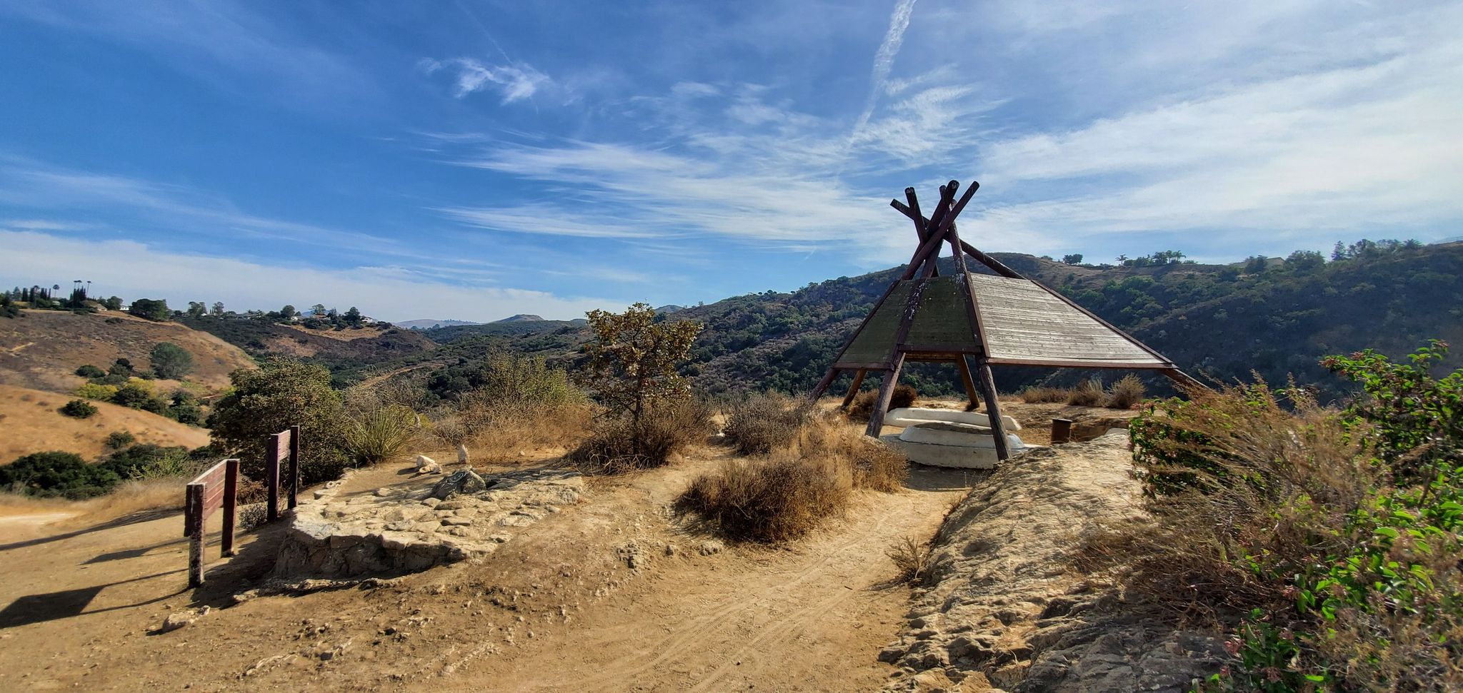 A teepee-like structure on a dirt path overlooking a hilly landscape under a blue sky. - Canejo Canyon Open Space Loop