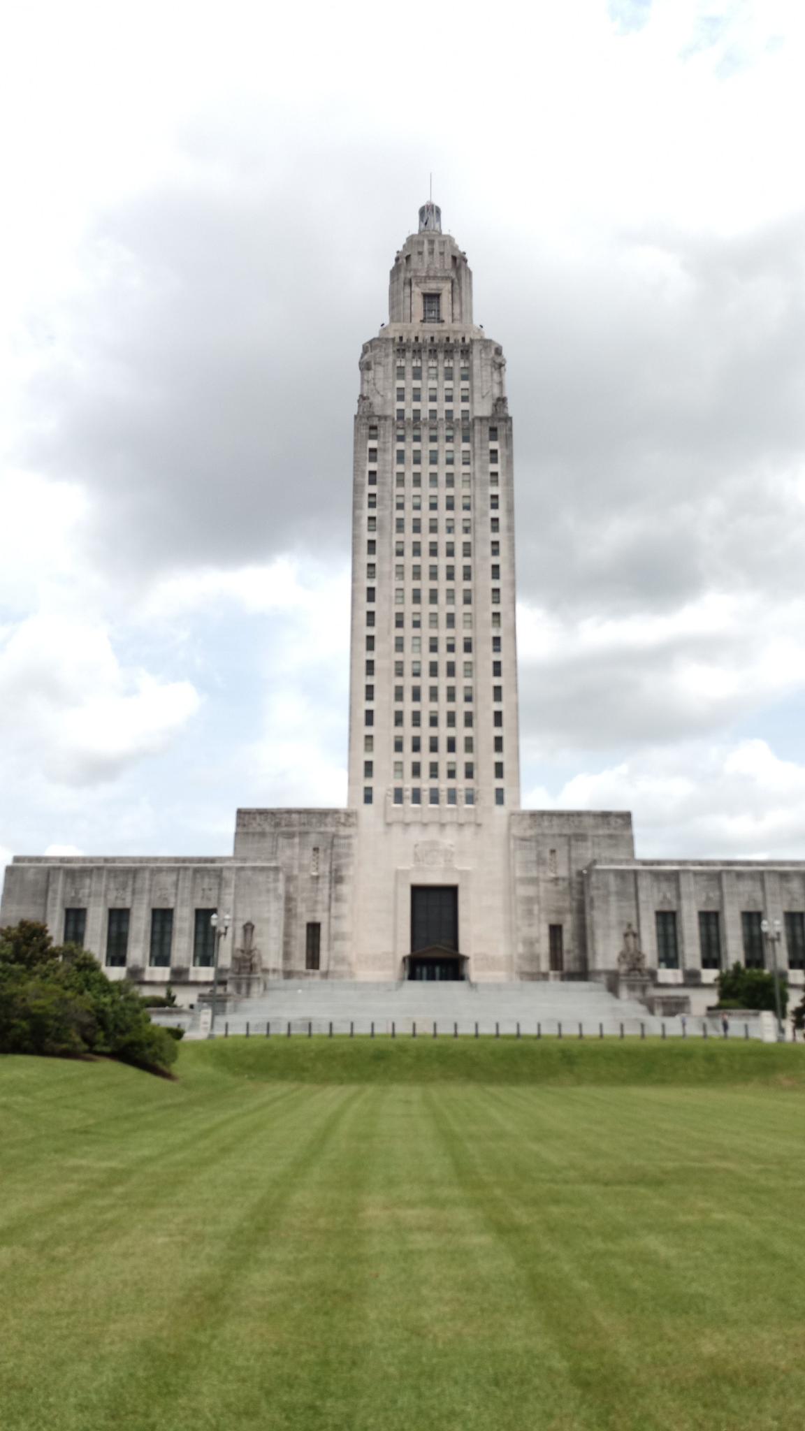 Tall, ornate building with a tower over a green lawn under an overcast sky.