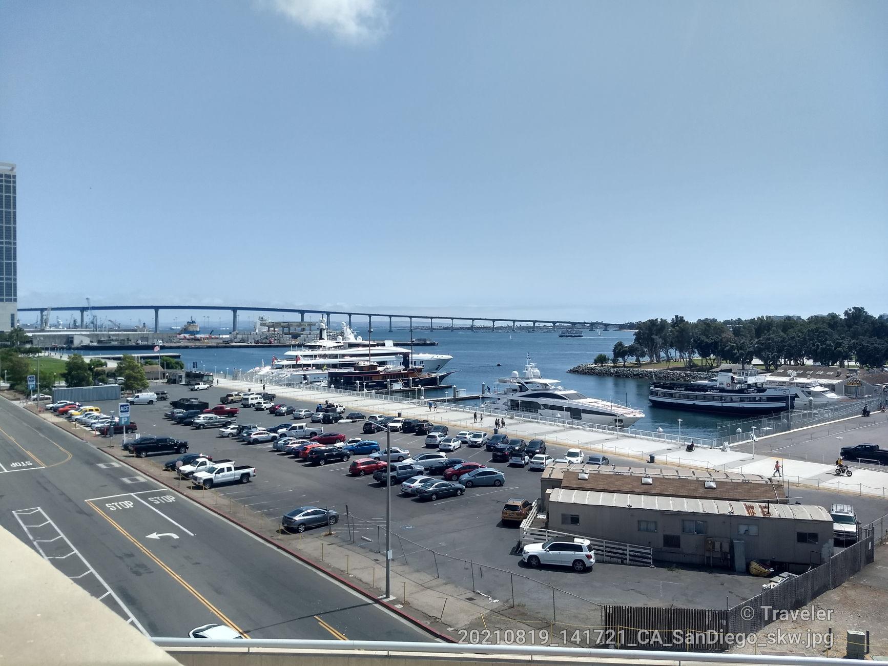Overhead view of a marina, parking lot, and distant bridge under clear skies.