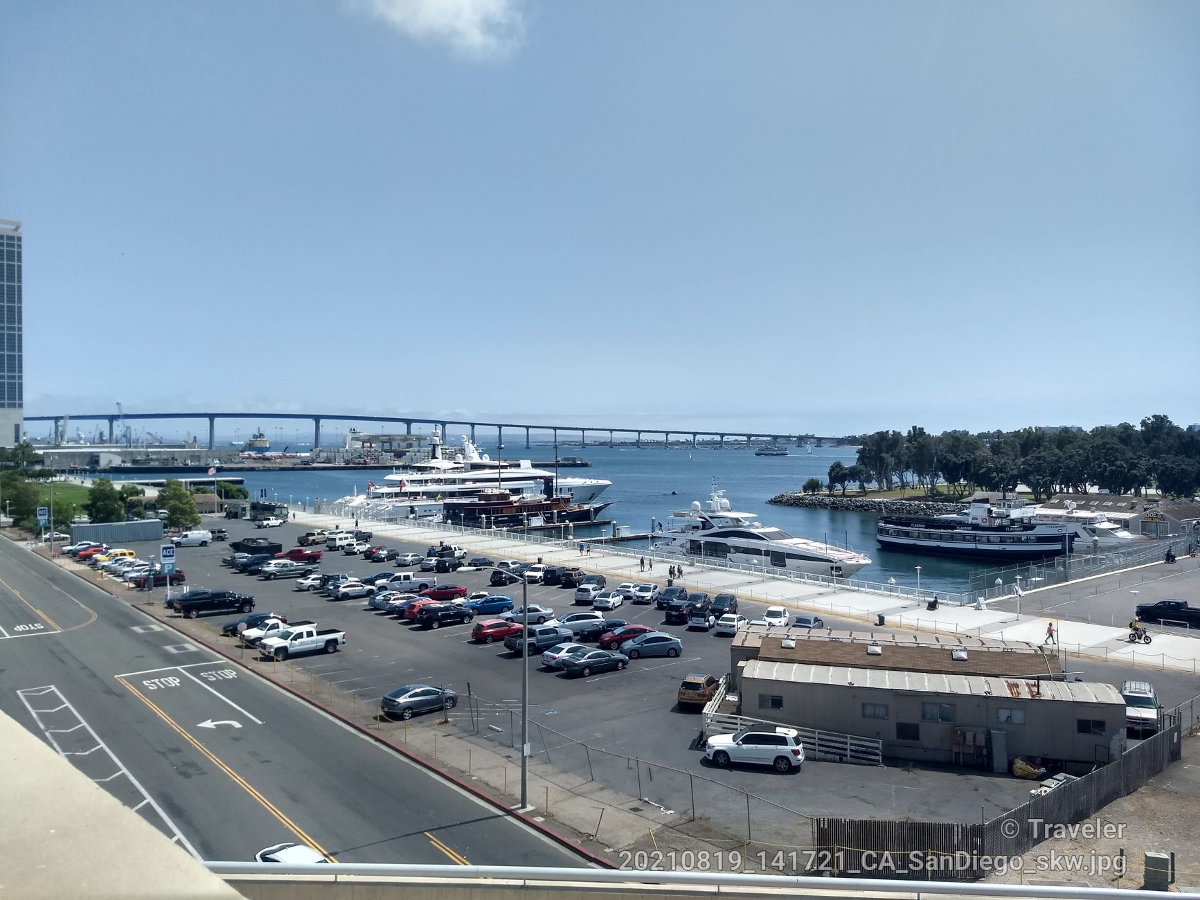 Overhead view of a marina, parking lot, and distant bridge under clear skies. - Embarcadero Marina Loop