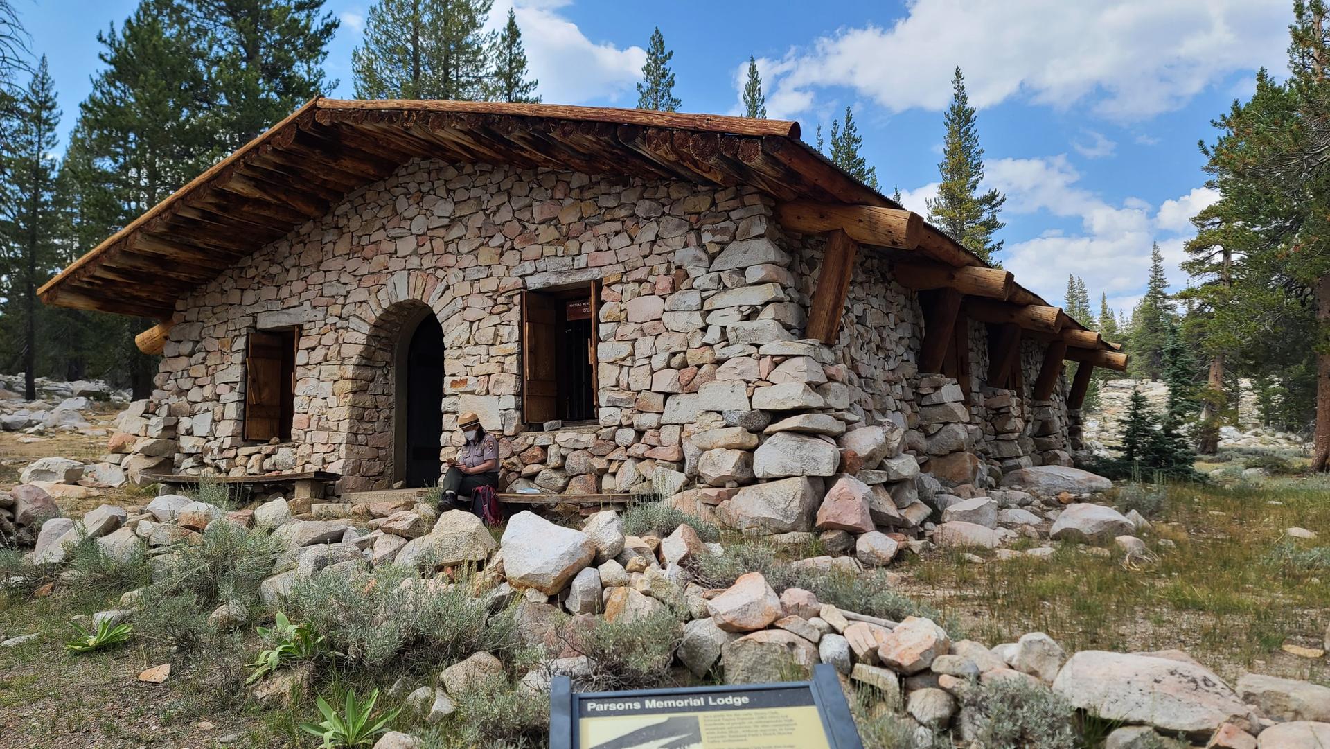 Stone lodge with a wooden roof, a person sitting outside on a sunny day.