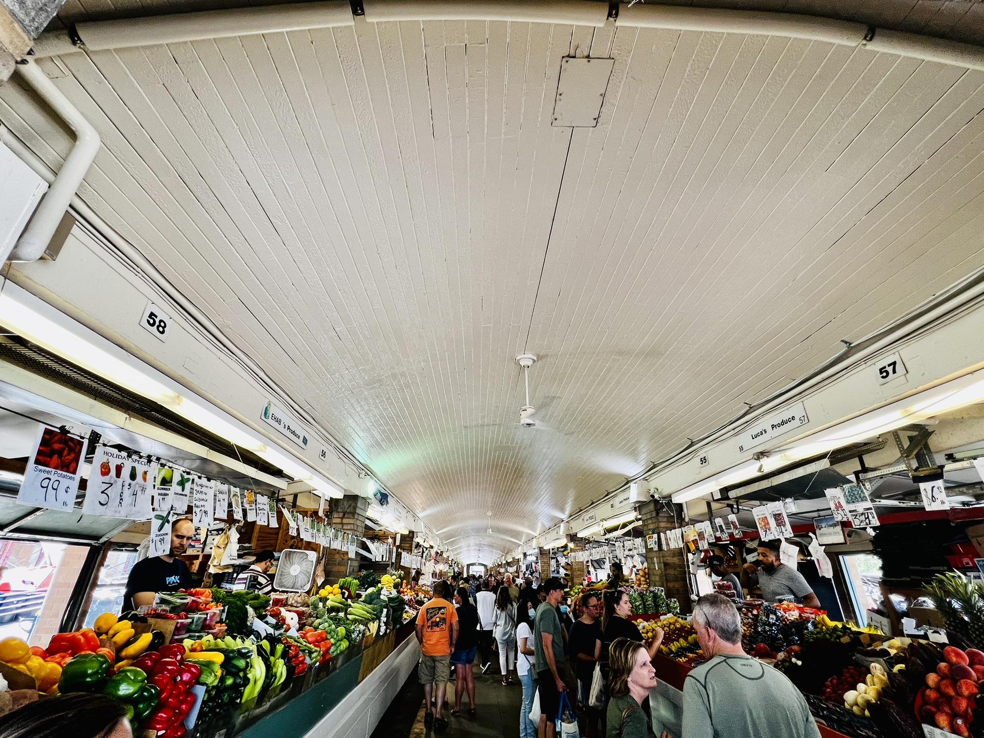 Busy indoor market aisle with many people and colorful produce stalls.
