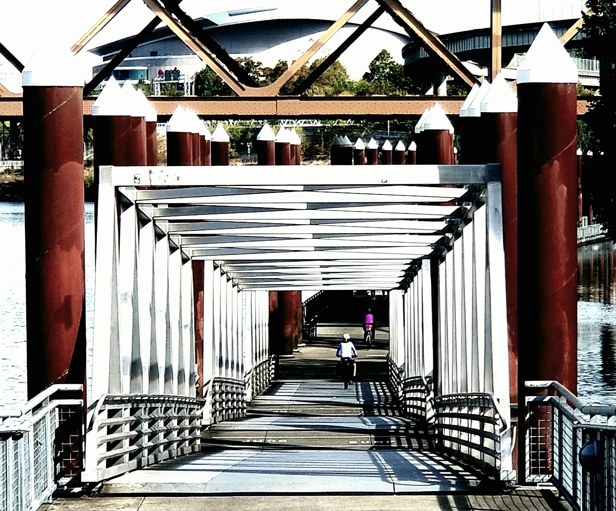 Two people cycle on a sunny, covered walkway over water. - Willamette and Columbia Rivers loop via the 40 Mile Loop trail