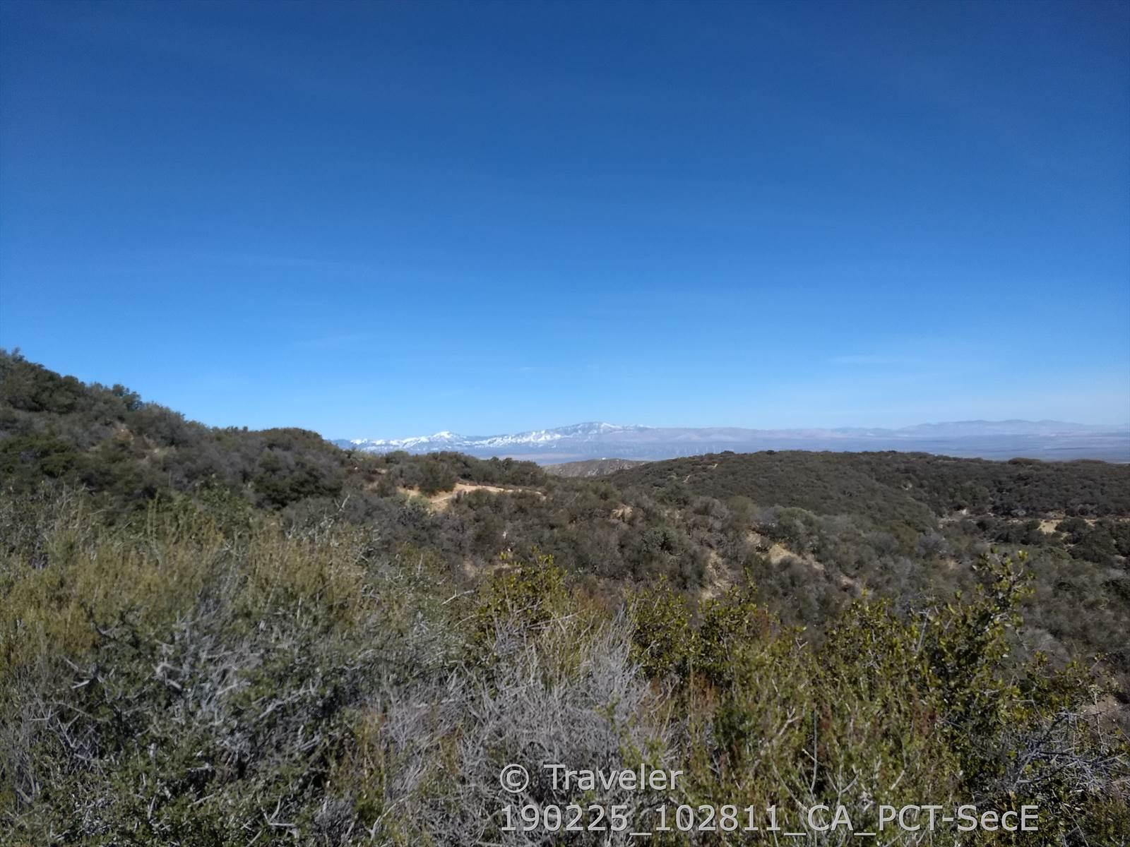 Scrubby hills in the foreground with distant snow-capped mountains under a clear sky.