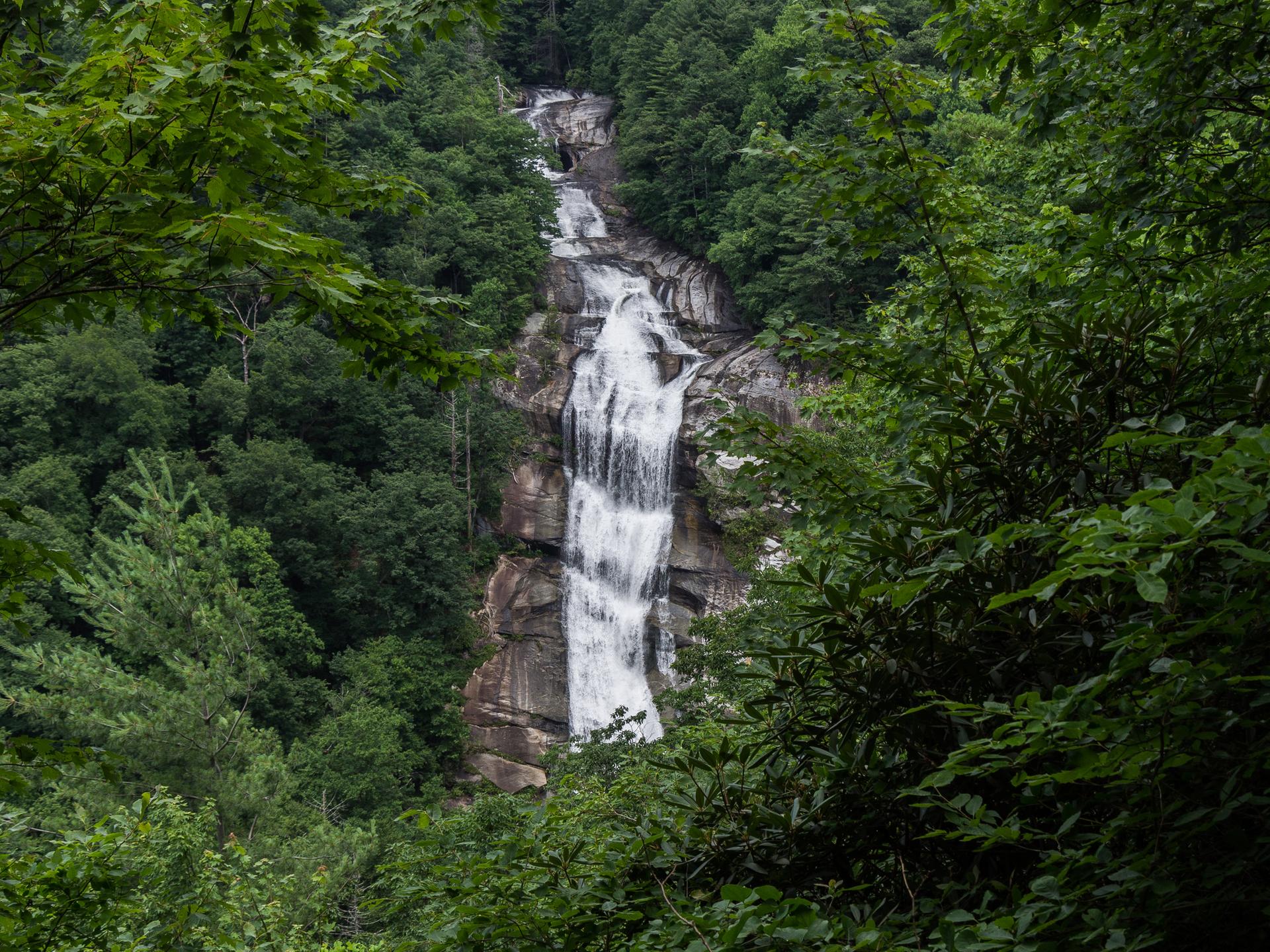 Tall waterfall cascading down a rocky cliff, framed by dense green forest.