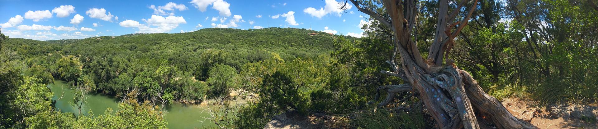 Panoramic view of a lush green valley with a river under a blue sky.