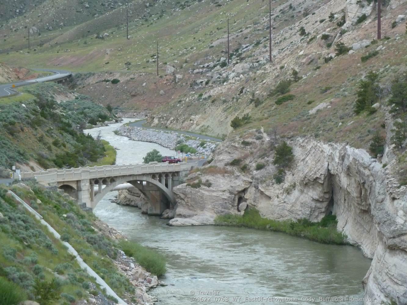 Stone bridge over a river in a green valley under a bright sky.