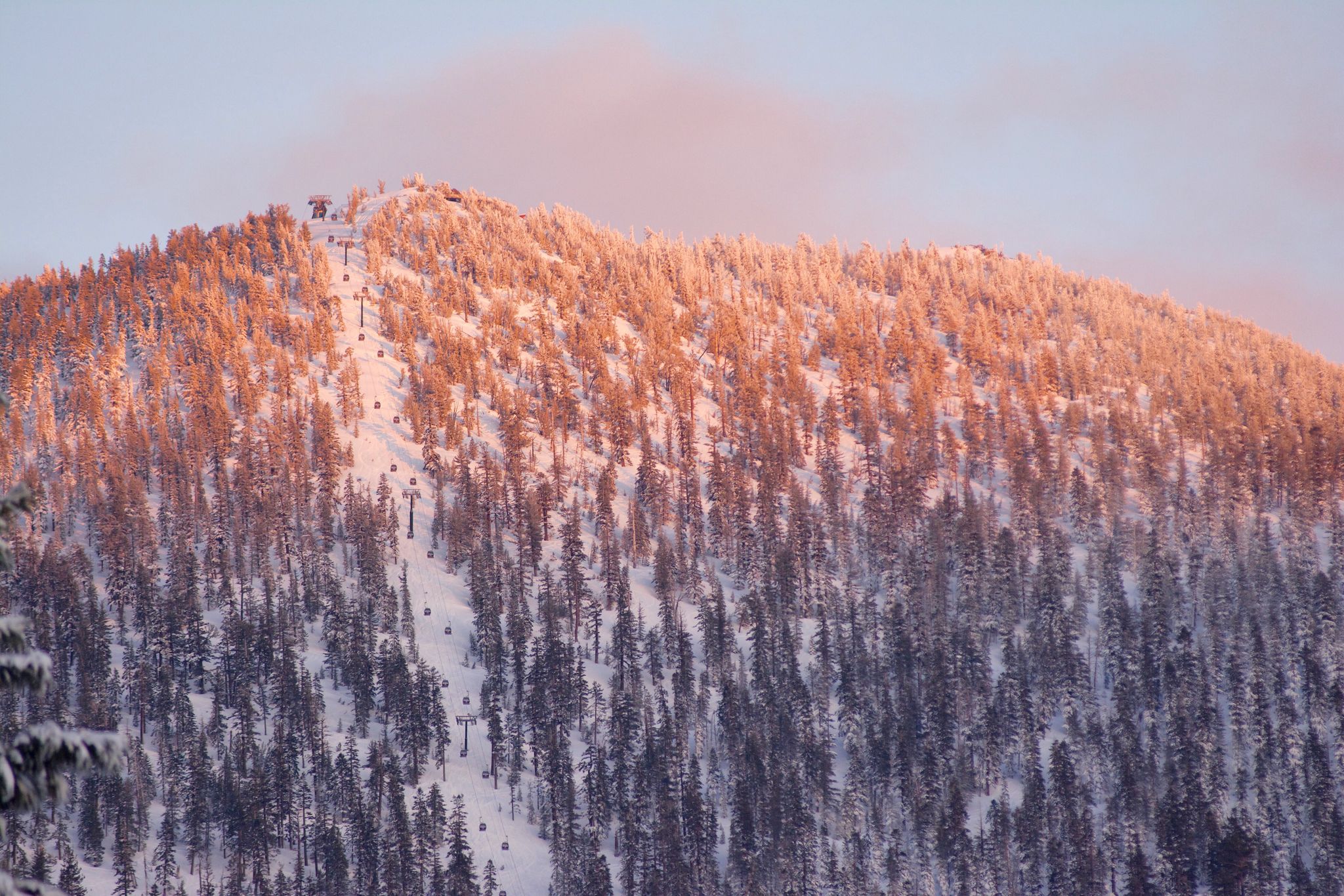 Snow-covered mountain with ski lifts, illuminated by warm golden hour light. - East Peak Hiking Trail