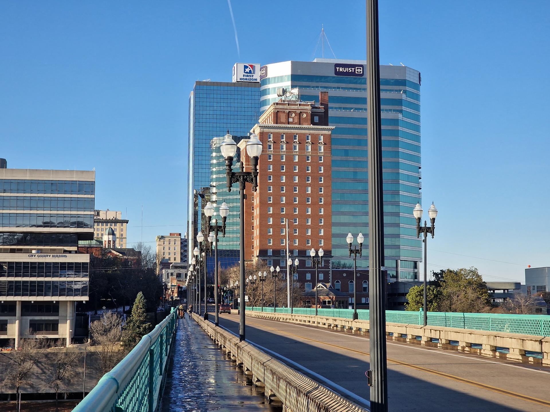 A city bridge with lampposts leads to tall buildings under a clear sky.