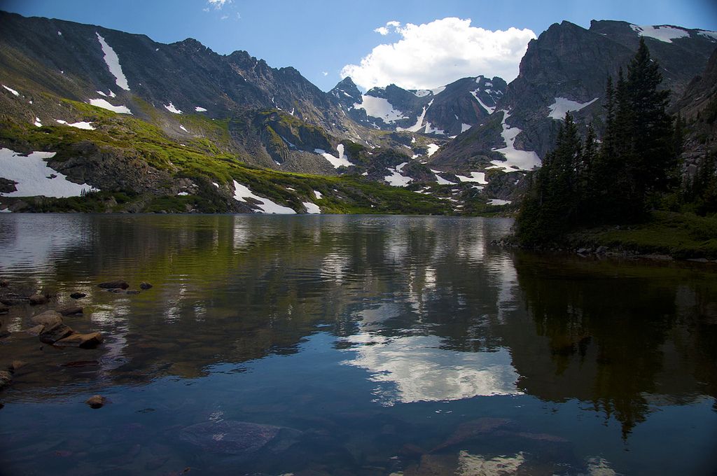 Sunny alpine lake reflecting clouds, surrounded by snow-dusted mountains and green slopes. - Lake Isabelle via Pawnee Pass Trail