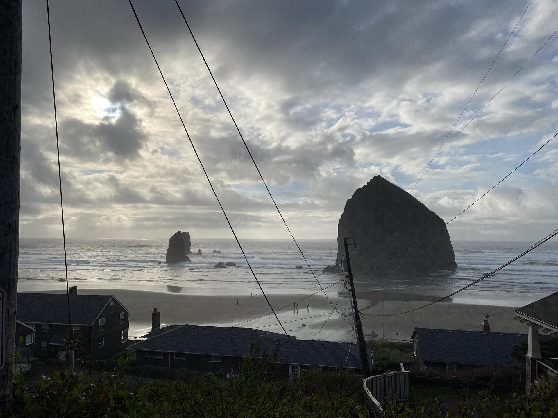 Dramatic cloudy sky over a large sea stack, beach, and coastal houses.