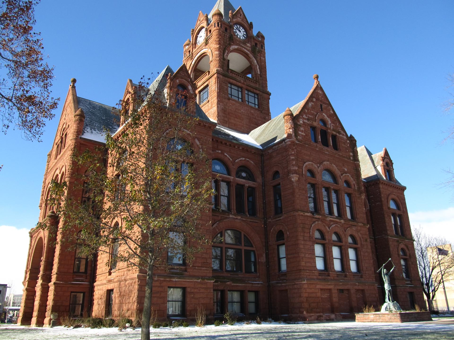 Grand red brick building with a tall clock tower under a clear blue sky.