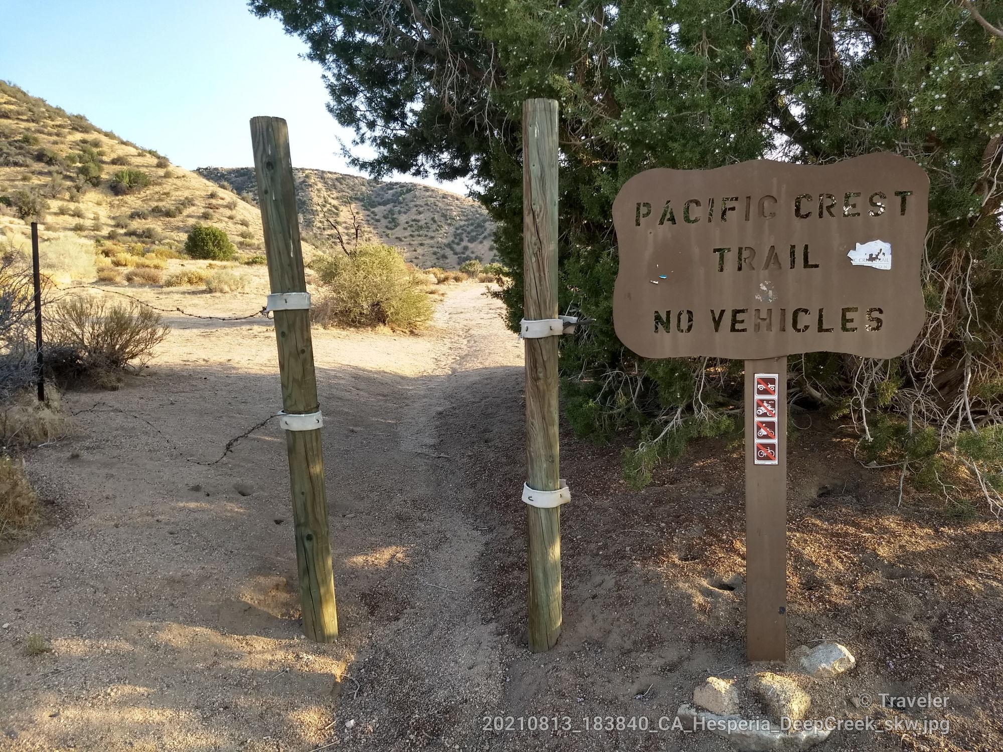 Wooden trail sign at a dirt path entrance, 'No Vehicles'.