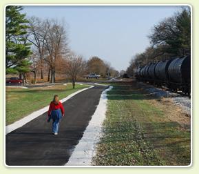 Person walks on a paved path beside parked train cars on a clear day.
