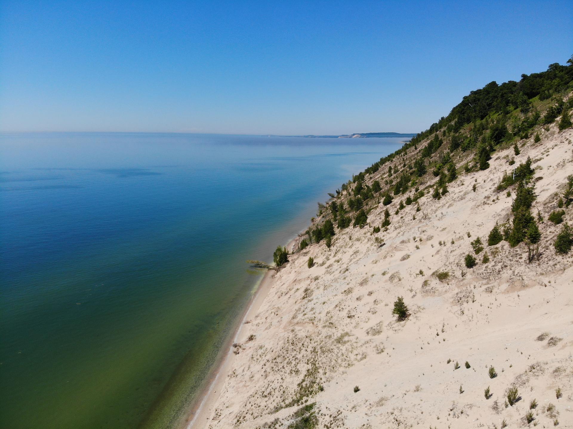 Expansive sandy dune slopes down to clear blue water under a bright sky.
