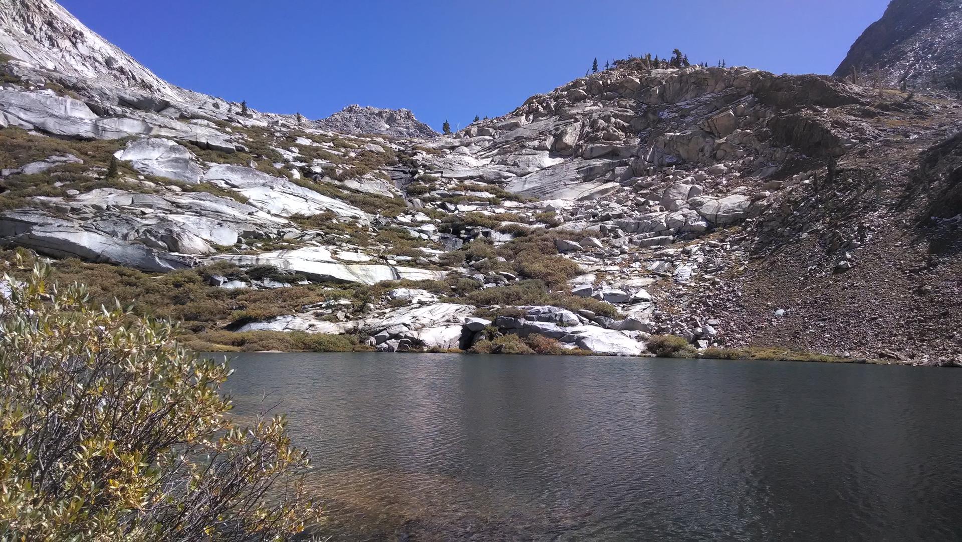 A calm mountain lake surrounded by rocky, barren slopes under a clear sky.