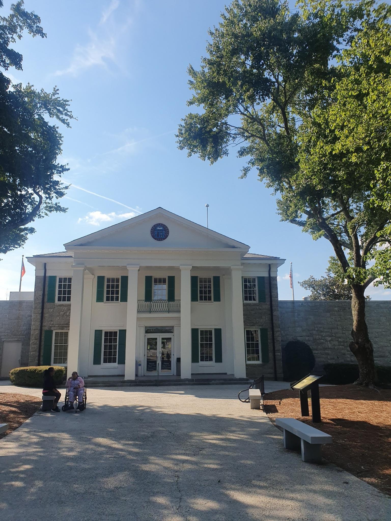 Grand white building with columns and green shutters under a clear blue sky.