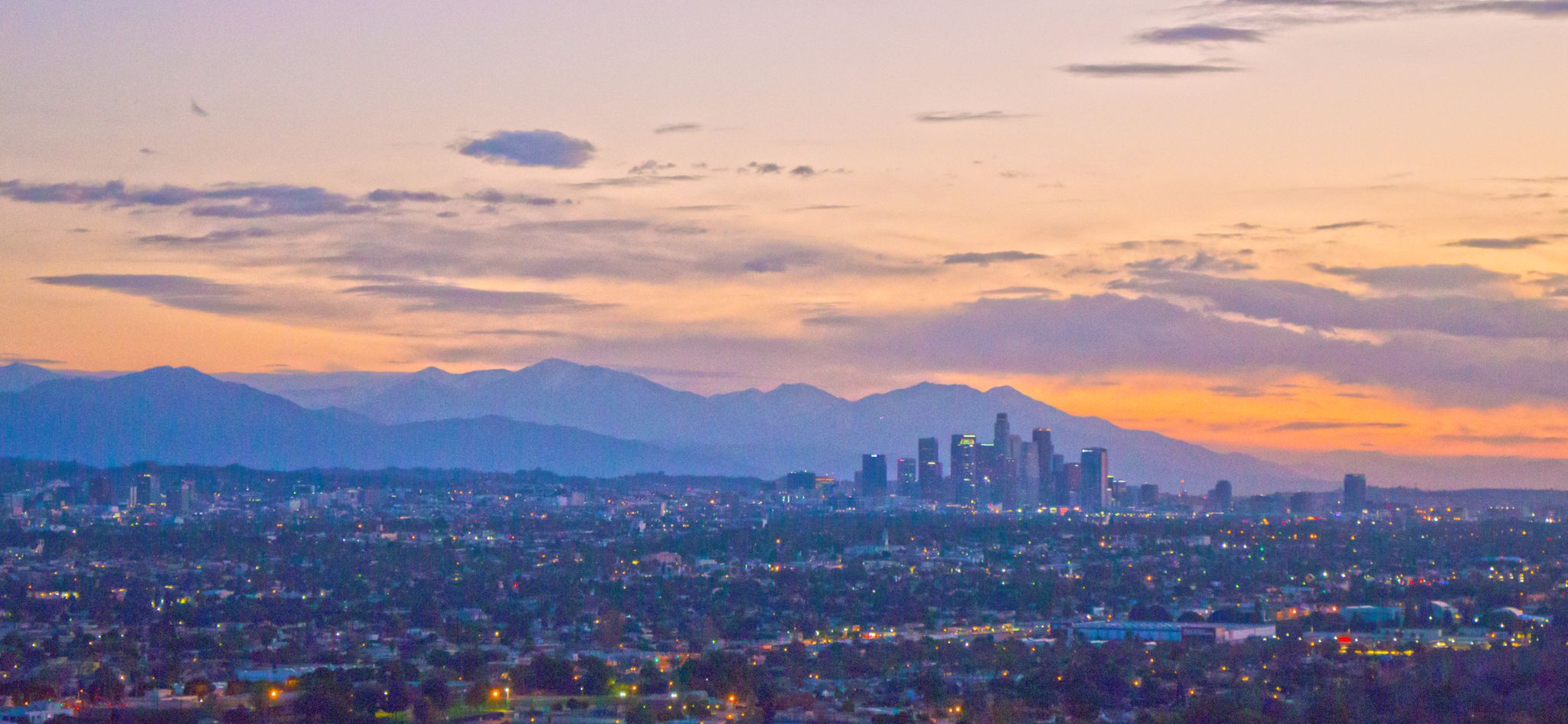 A city skyline and distant mountains at sunset with orange and purple clouds. - Baldwin Hills loop from NPR West