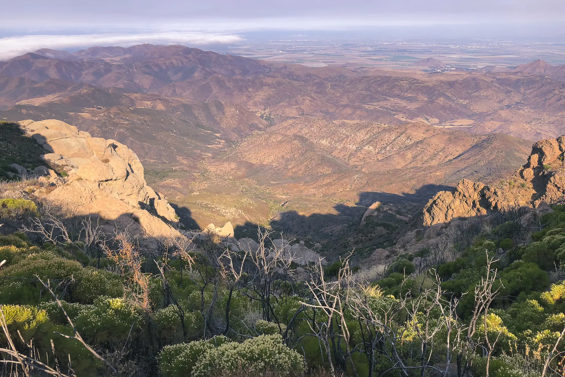 Panoramic view of a rugged mountain valley with distant plains under golden light.