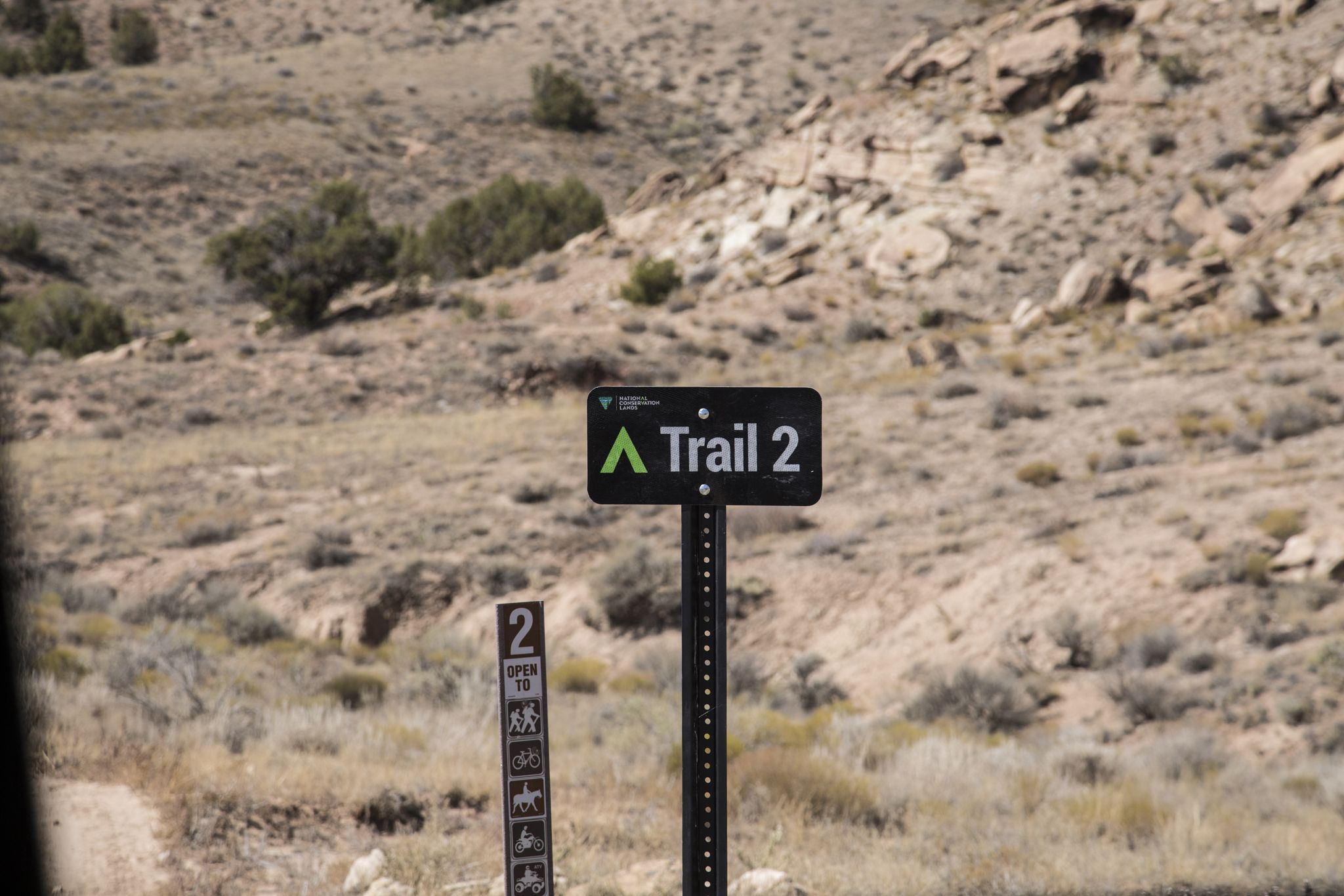 A black trail sign with green text 'Trail 2' on a dry hillside. - Western Rim Trail
