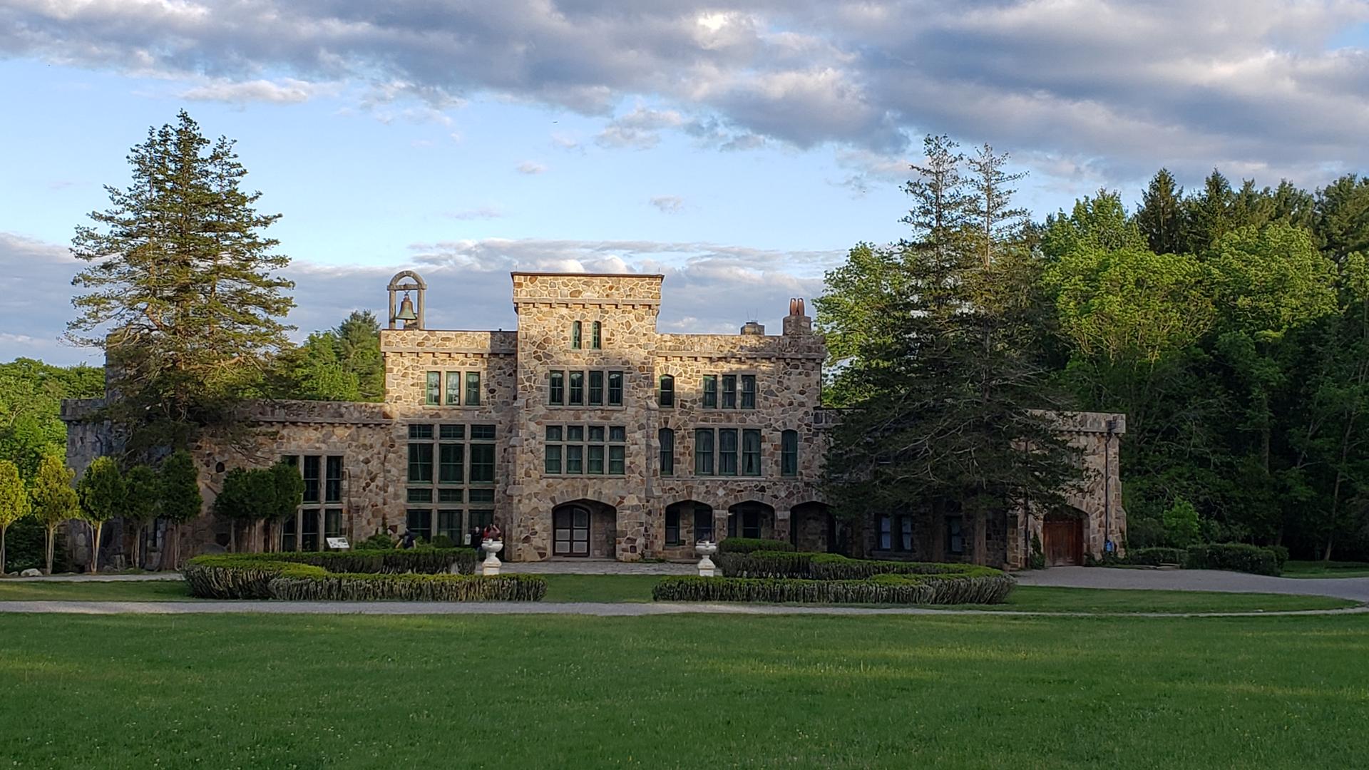 Grand stone castle-like building with green lawn under a partly cloudy sky.