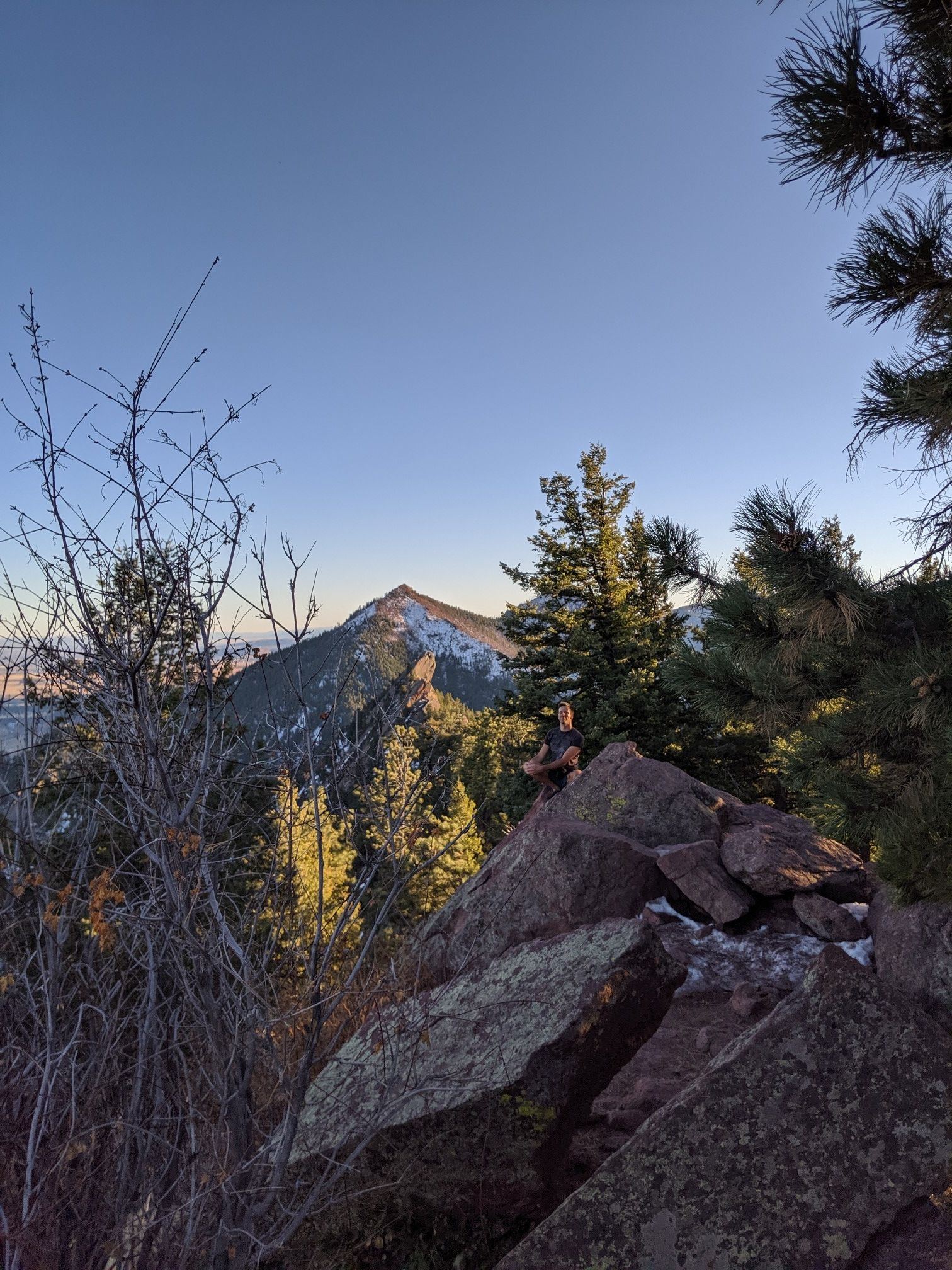 Mountain peak at sunrise, framed by pine trees and rocks, under a clear sky. - Green Mountain West Ridge Trail