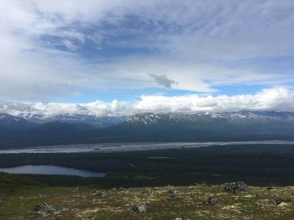 Panoramic view of a wide river valley, distant snowy mountains under cloudy sky.