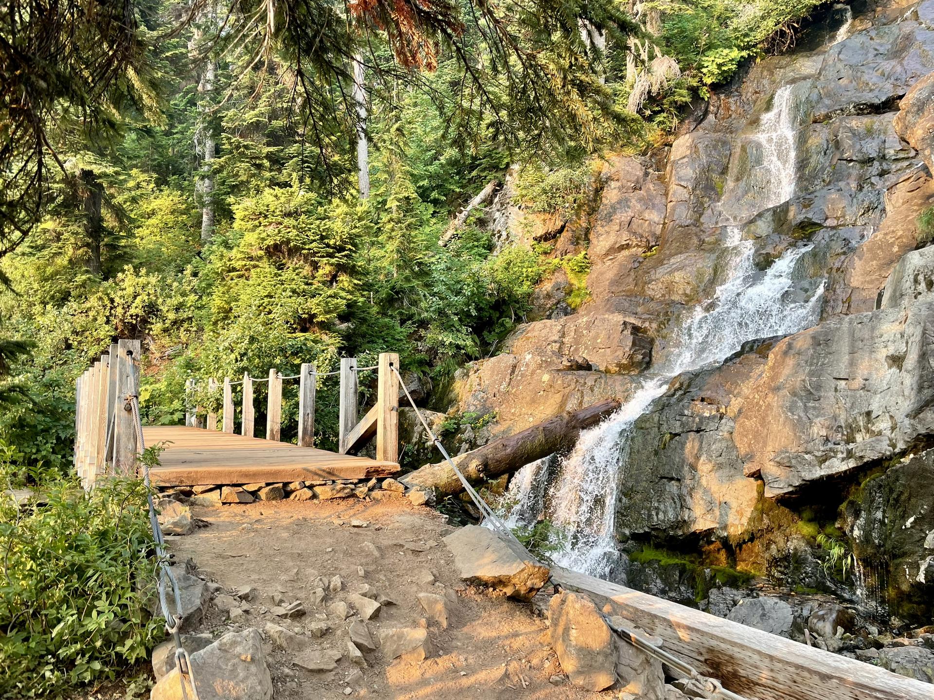 Wooden bridge beside a cascading waterfall in warm, golden light.