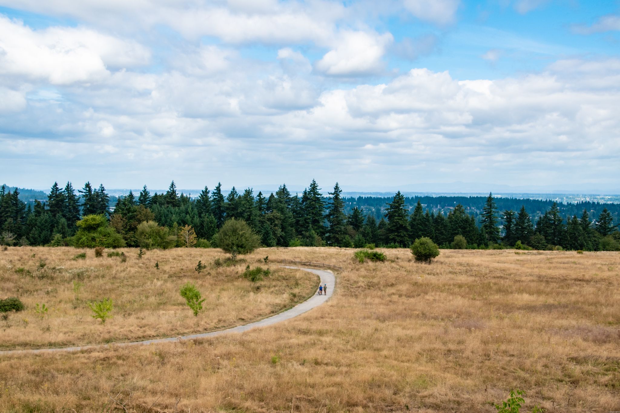 Two people walk on a winding dirt path through a vast dry field. - Short MTB Loop