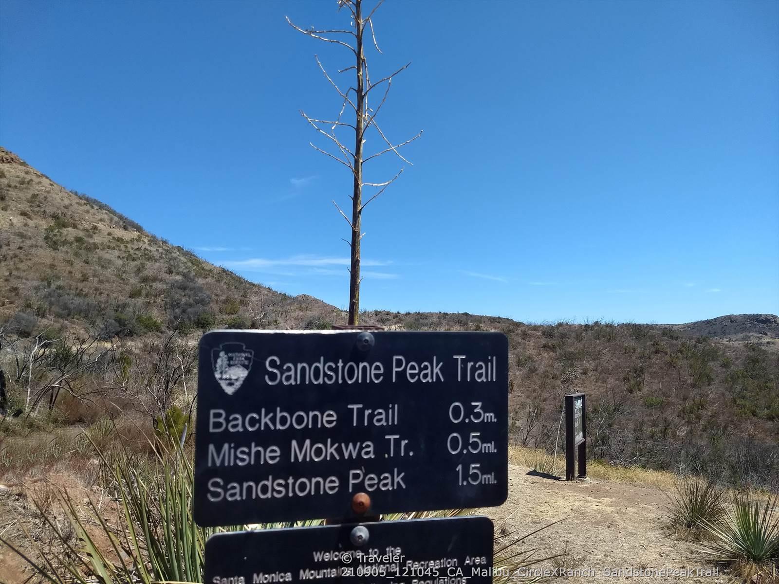 A trail sign stands on a dry hill under a clear blue sky.