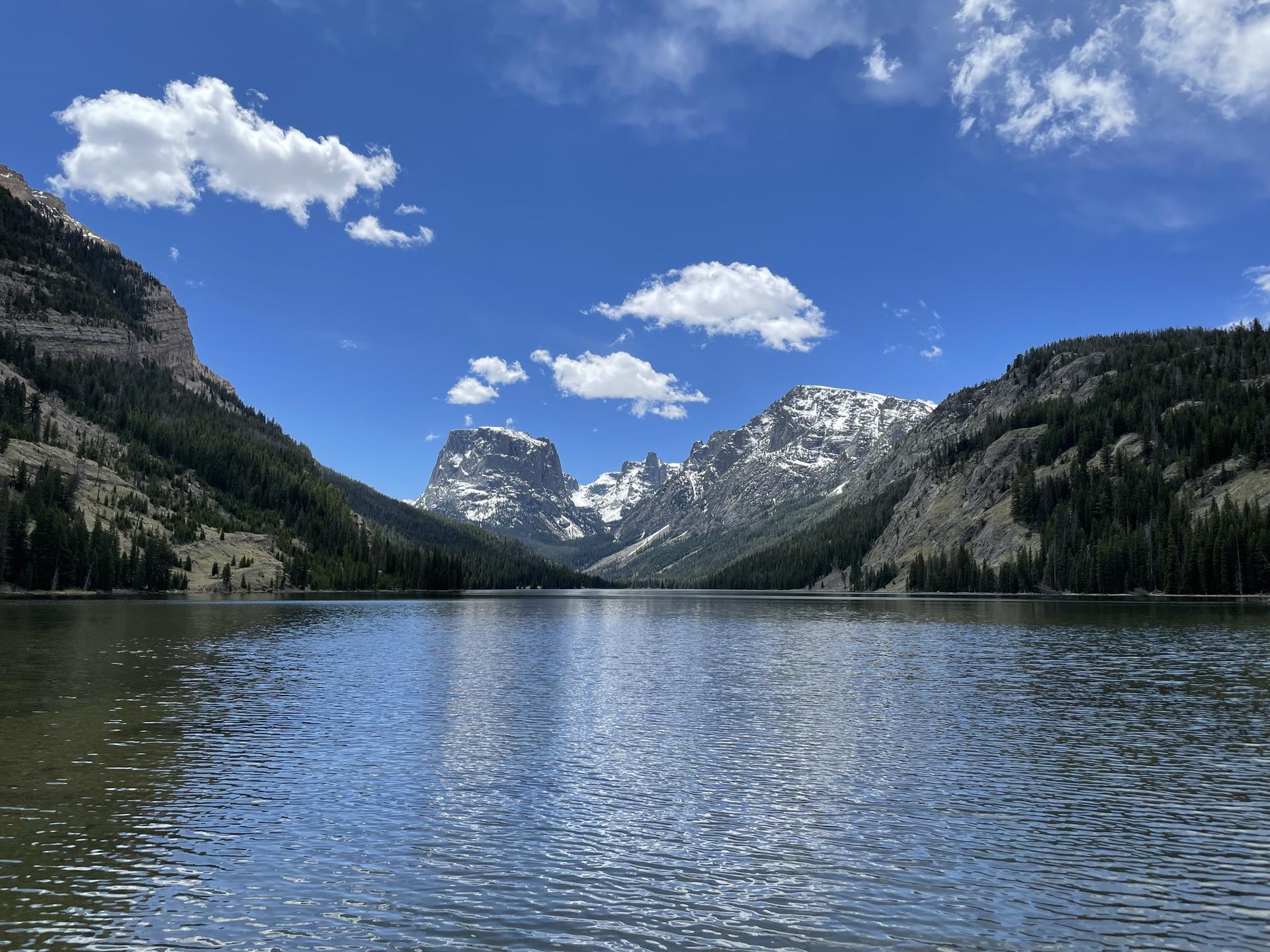 Large lake surrounded by towering, snow-capped mountains under a bright sky.