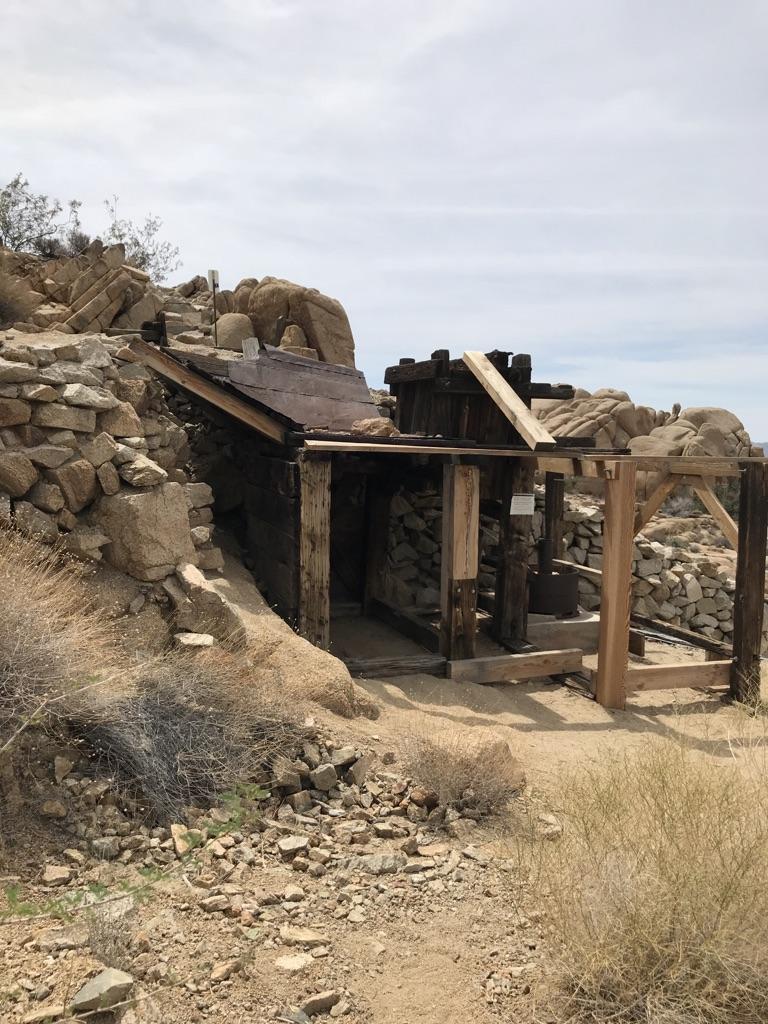 Old wooden structure built into rocky desert landscape under an overcast sky.