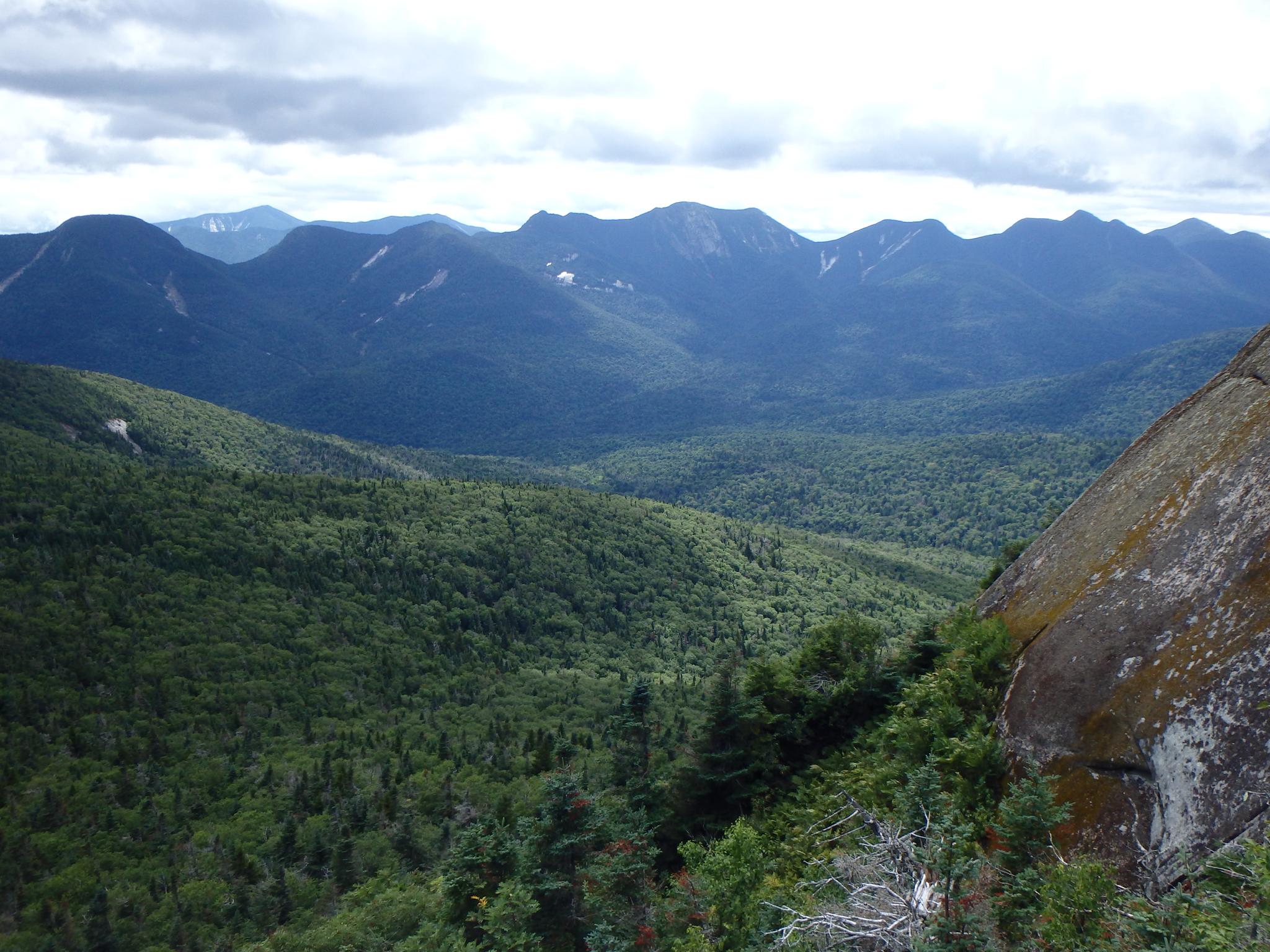 Expansive view of forested mountains and valleys under a cloudy sky.