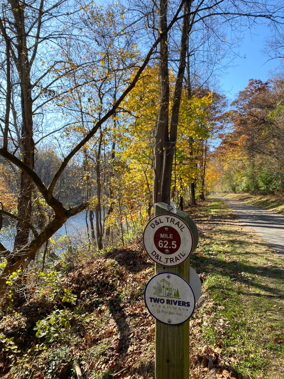 Trail signs on a post beside a river with autumn trees.