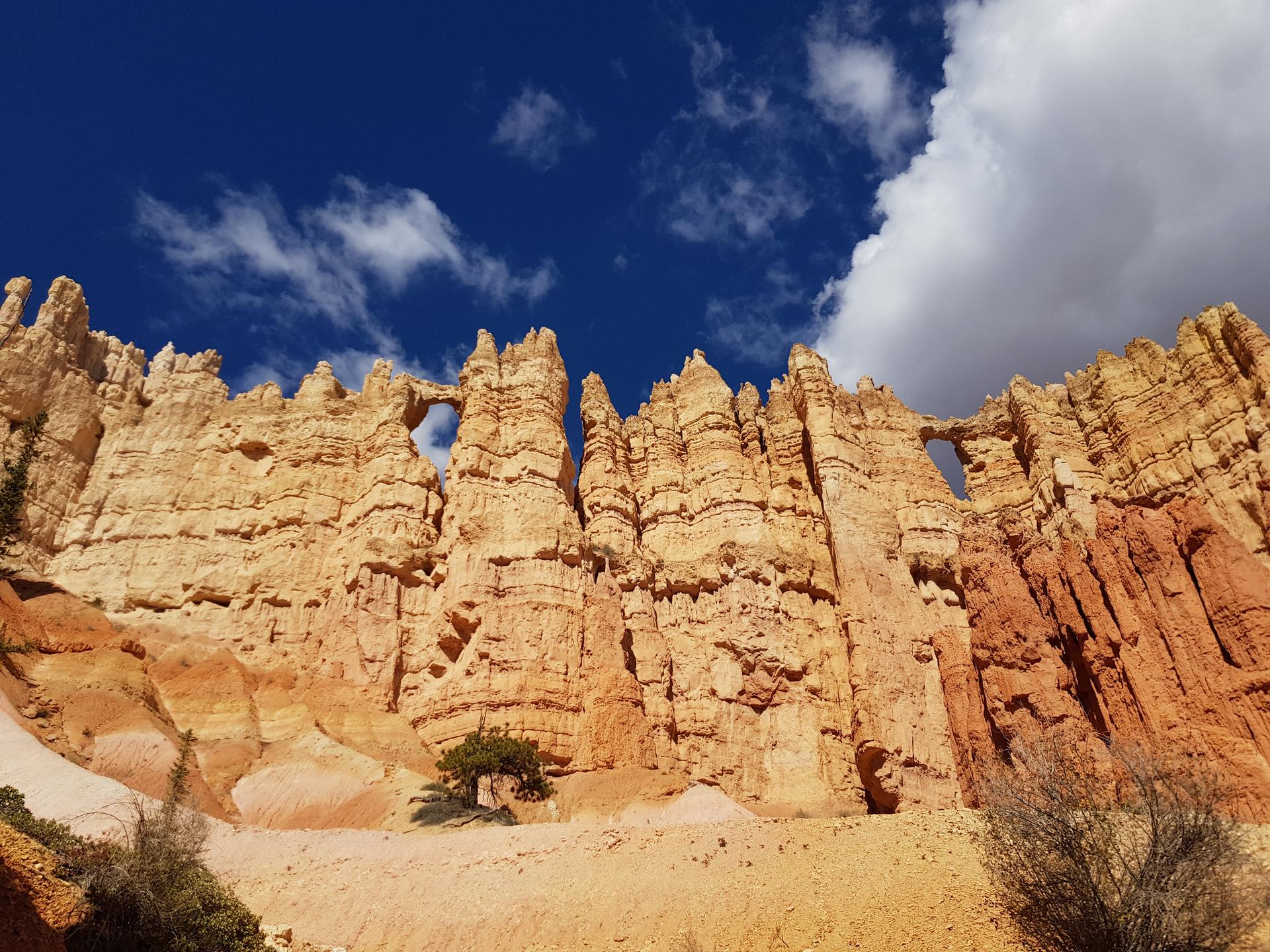Tall, layered orange rock formations with natural arches under a blue sky.