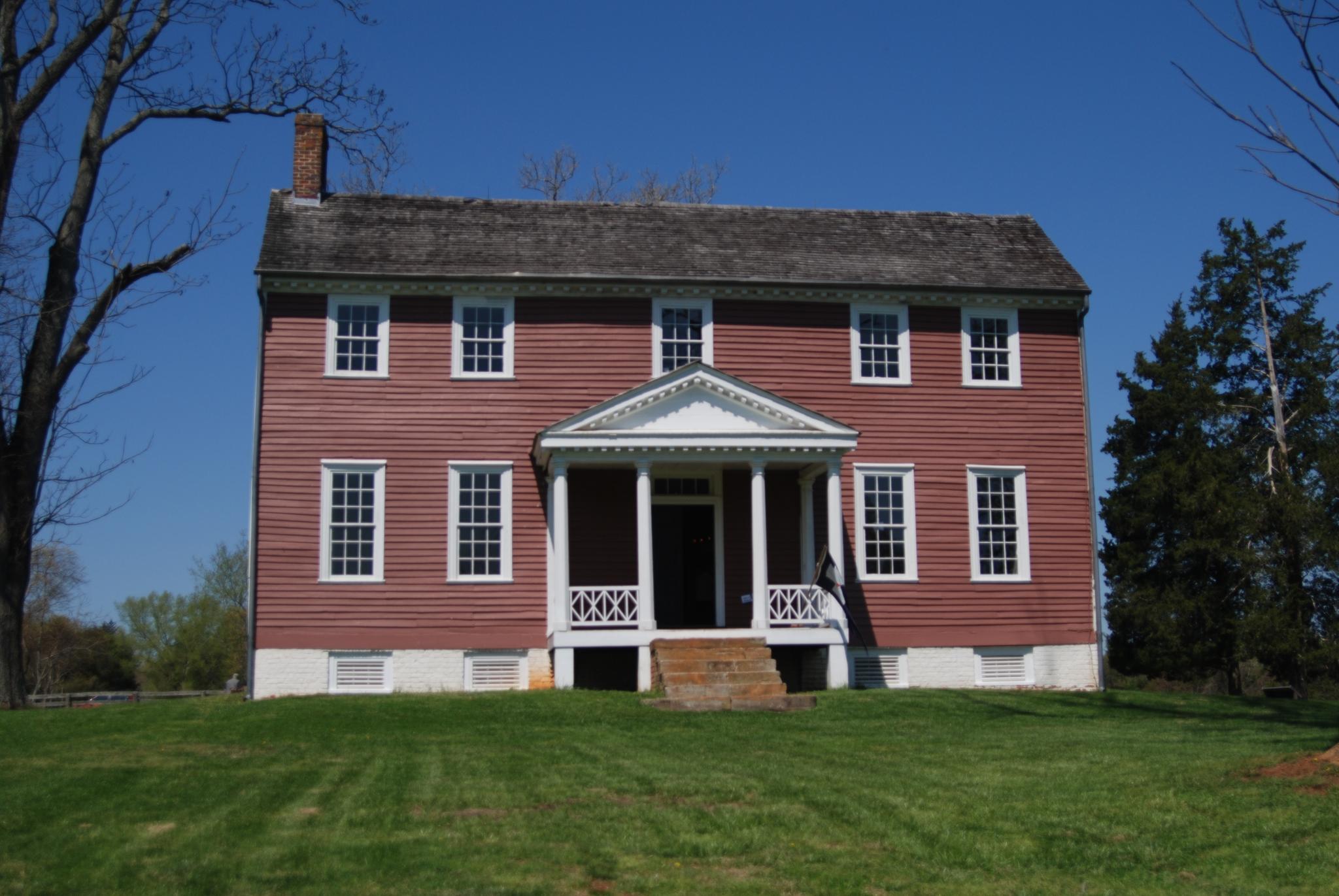 Red historic house with white trim on a green lawn under clear sky.