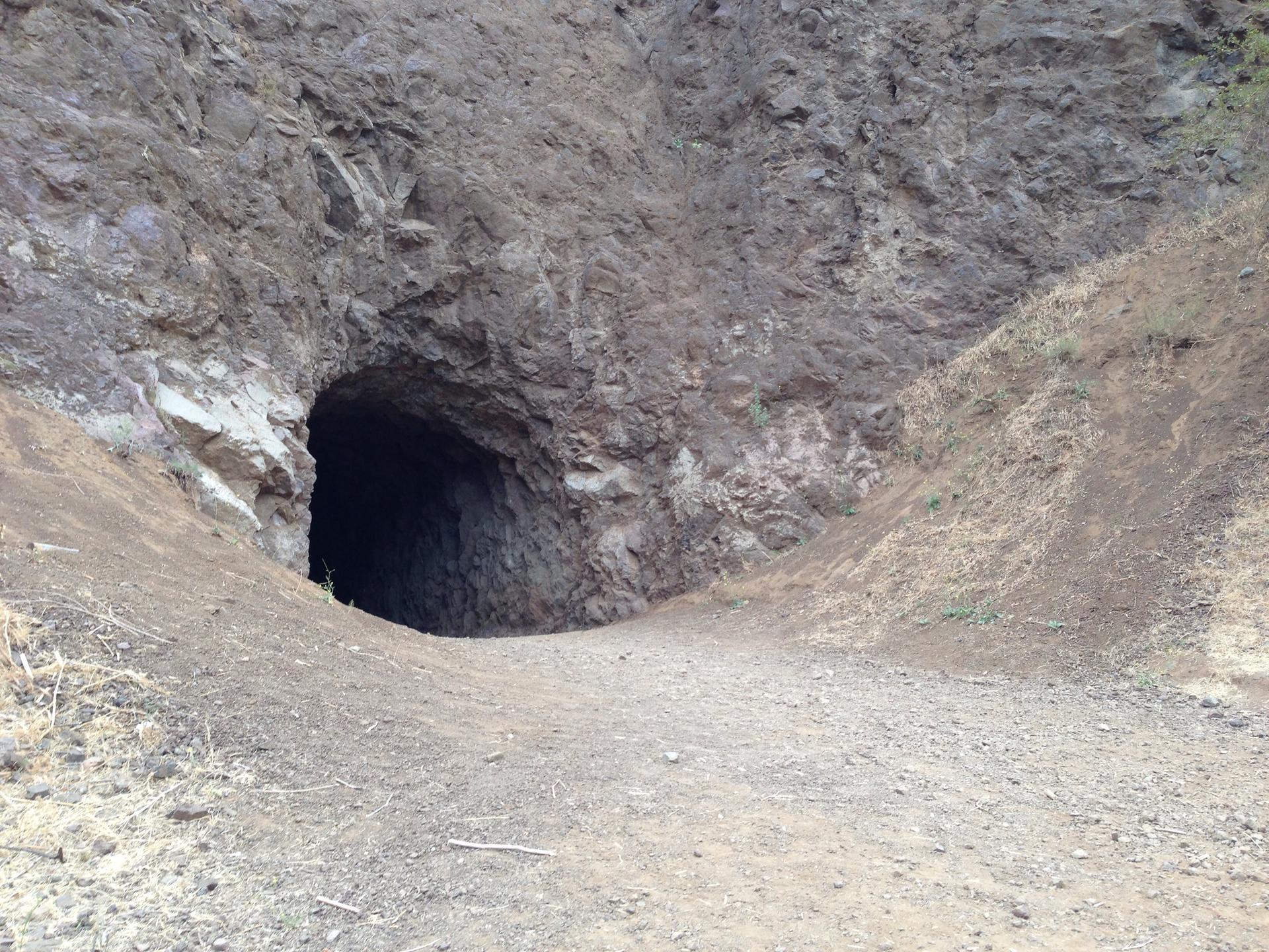 A dark cave entrance in a rocky hillside with a dirt path leading in.