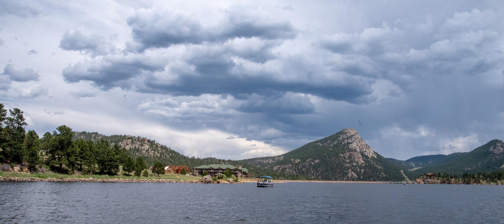 Dark lake with a small boat, mountains, and dense clouds overhead.