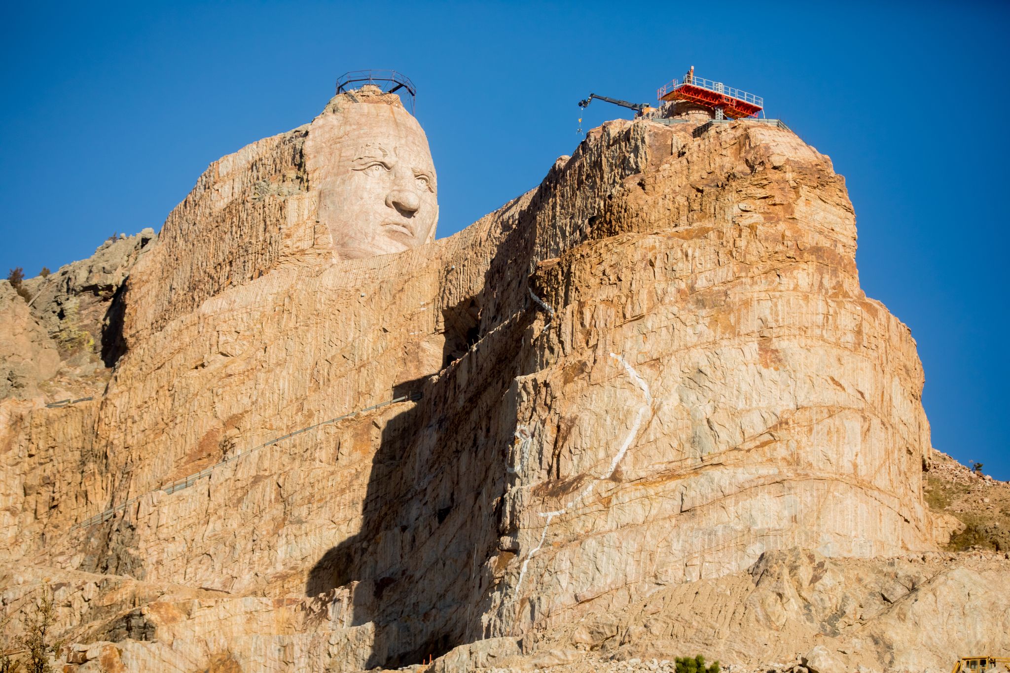 Massive rock carving of a face on a mountain, with construction equipment visible. - George S. Mickelson Trail to Stockade Lake