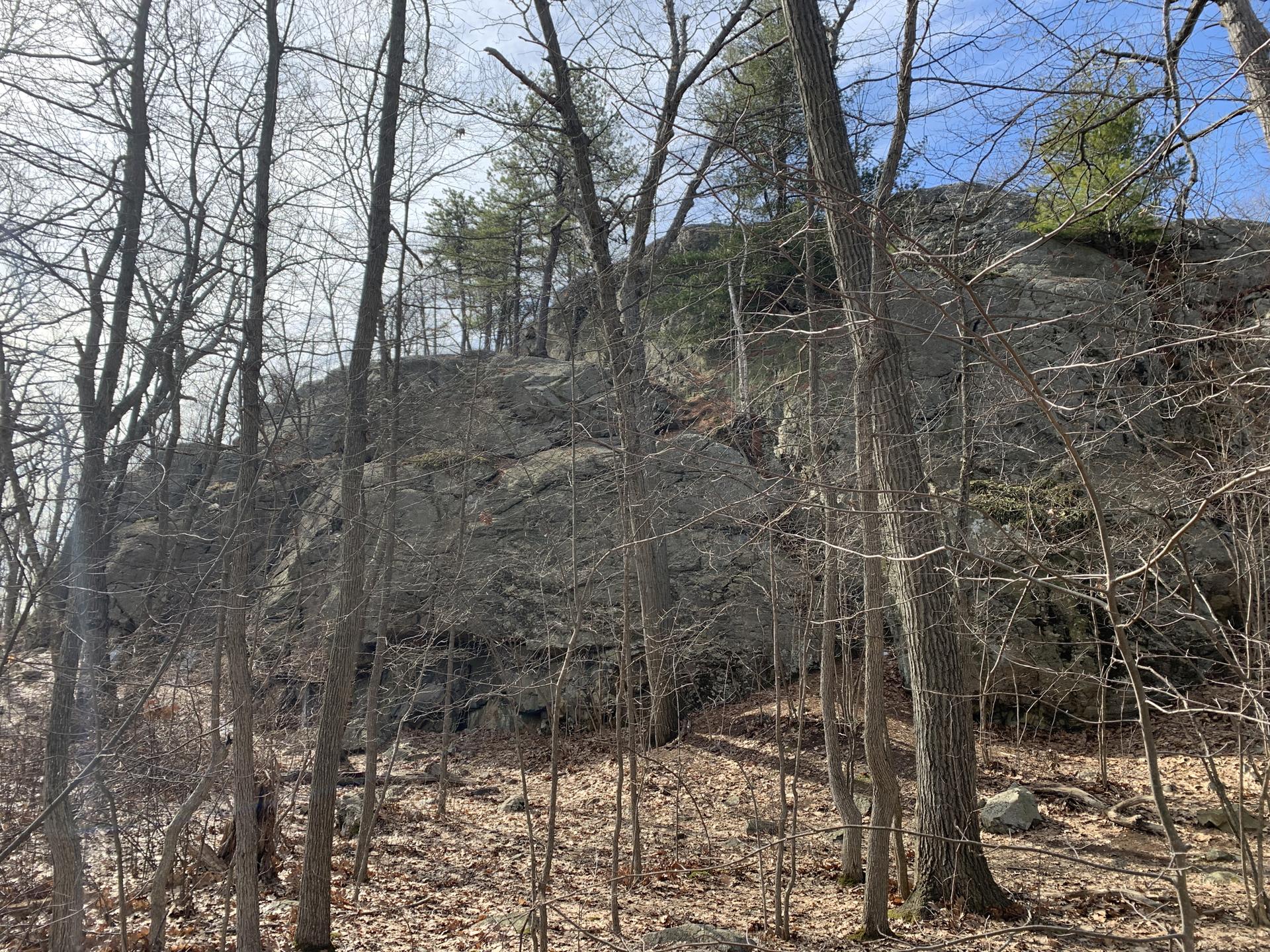 Large rocky outcrop and bare trees under a bright sky.