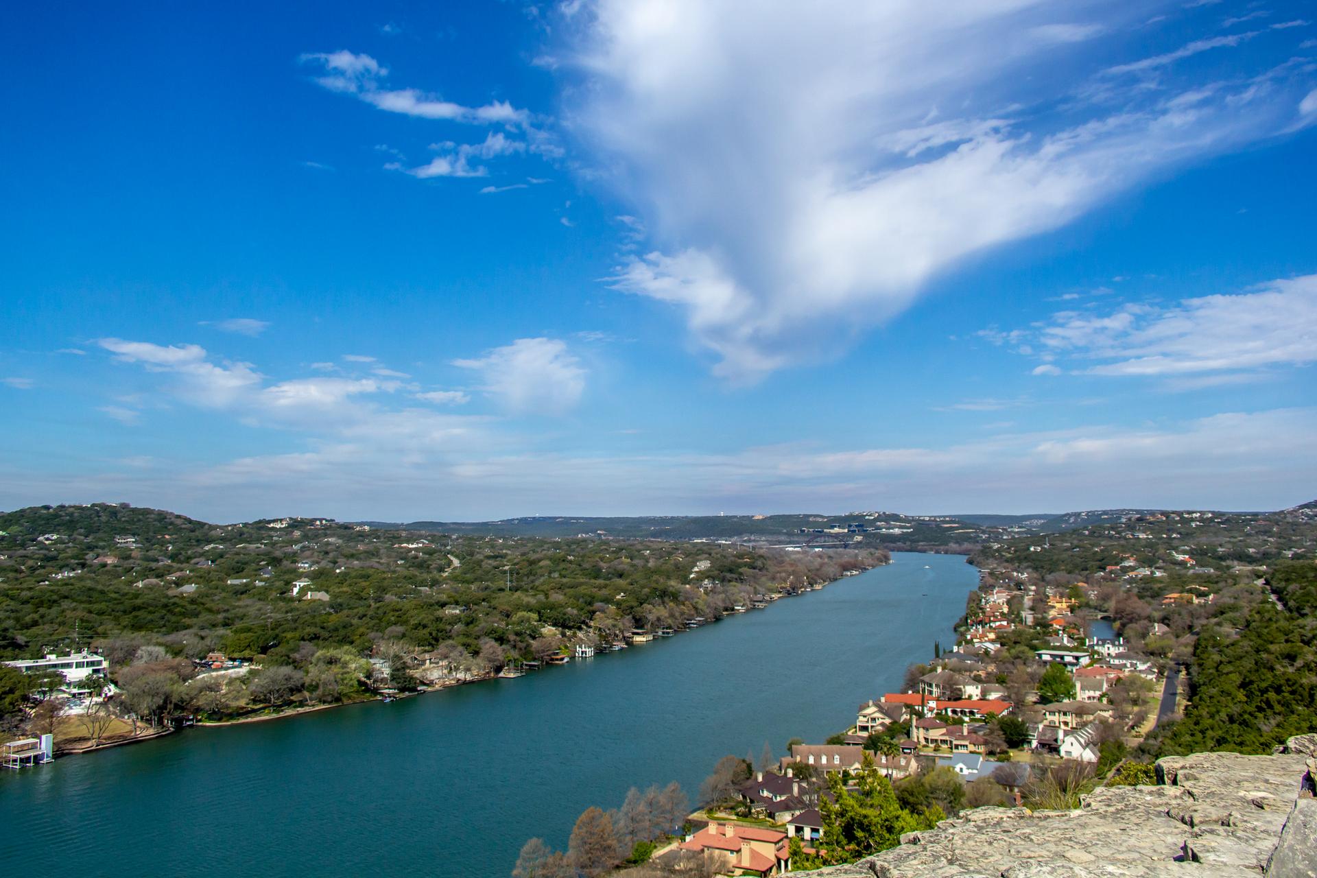 Panoramic view of a wide river winding through green hills with houses.
