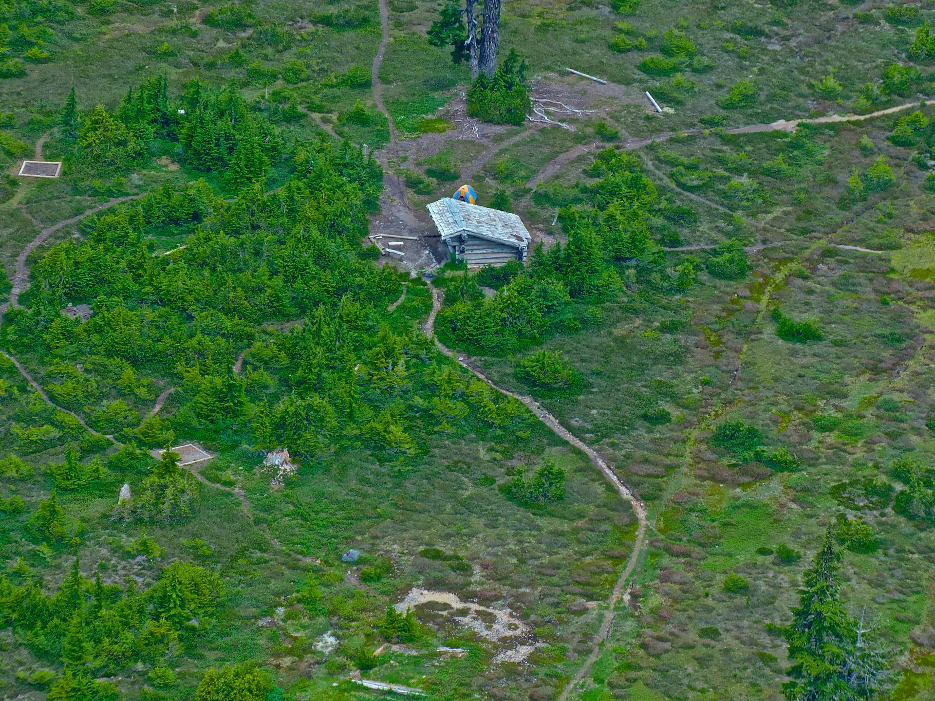 Aerial view of a small cabin nestled in a green, winding landscape.