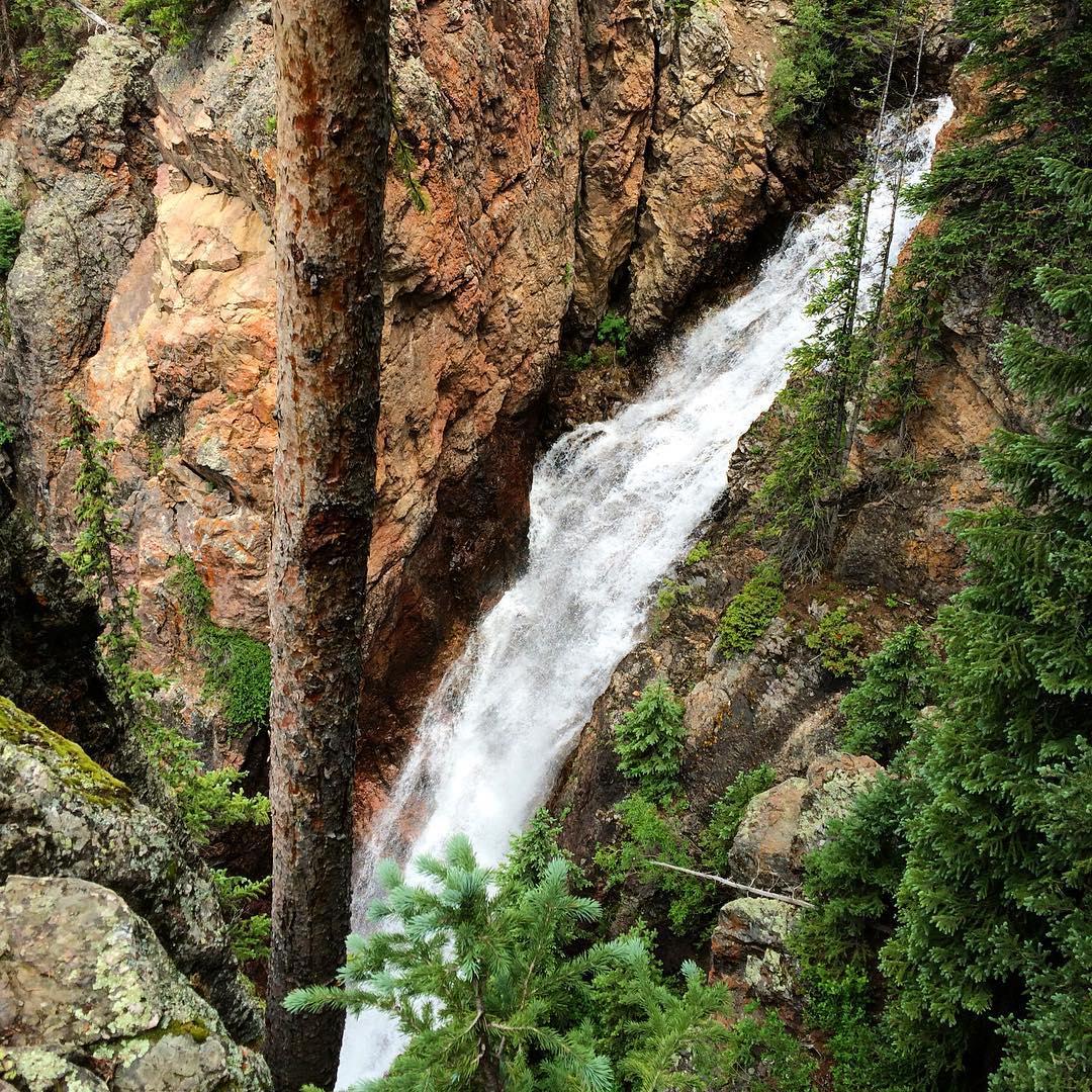 Powerful waterfall cascades down a rocky cliff amidst green trees.